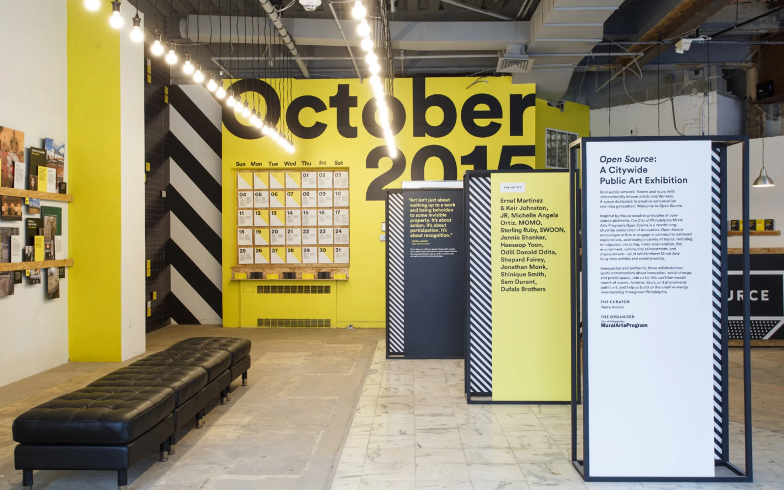 Photograph of the Open Source Hub, featuring a wall that is painted in yellow with a large-scale calendar of events and large, vinyl letters reading October 2015