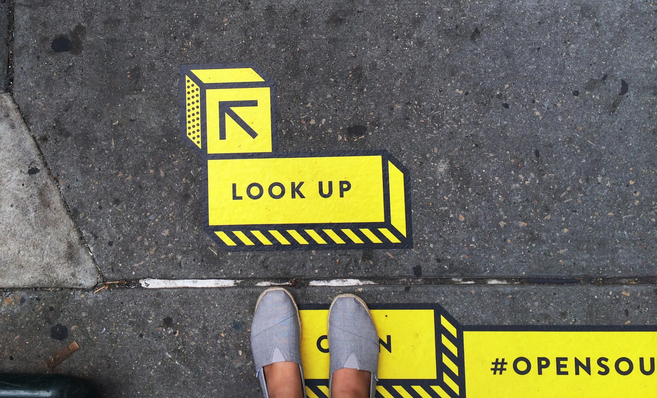 Photography of sidewalk with black and yellow ground vinyl from the Open Source exhibition