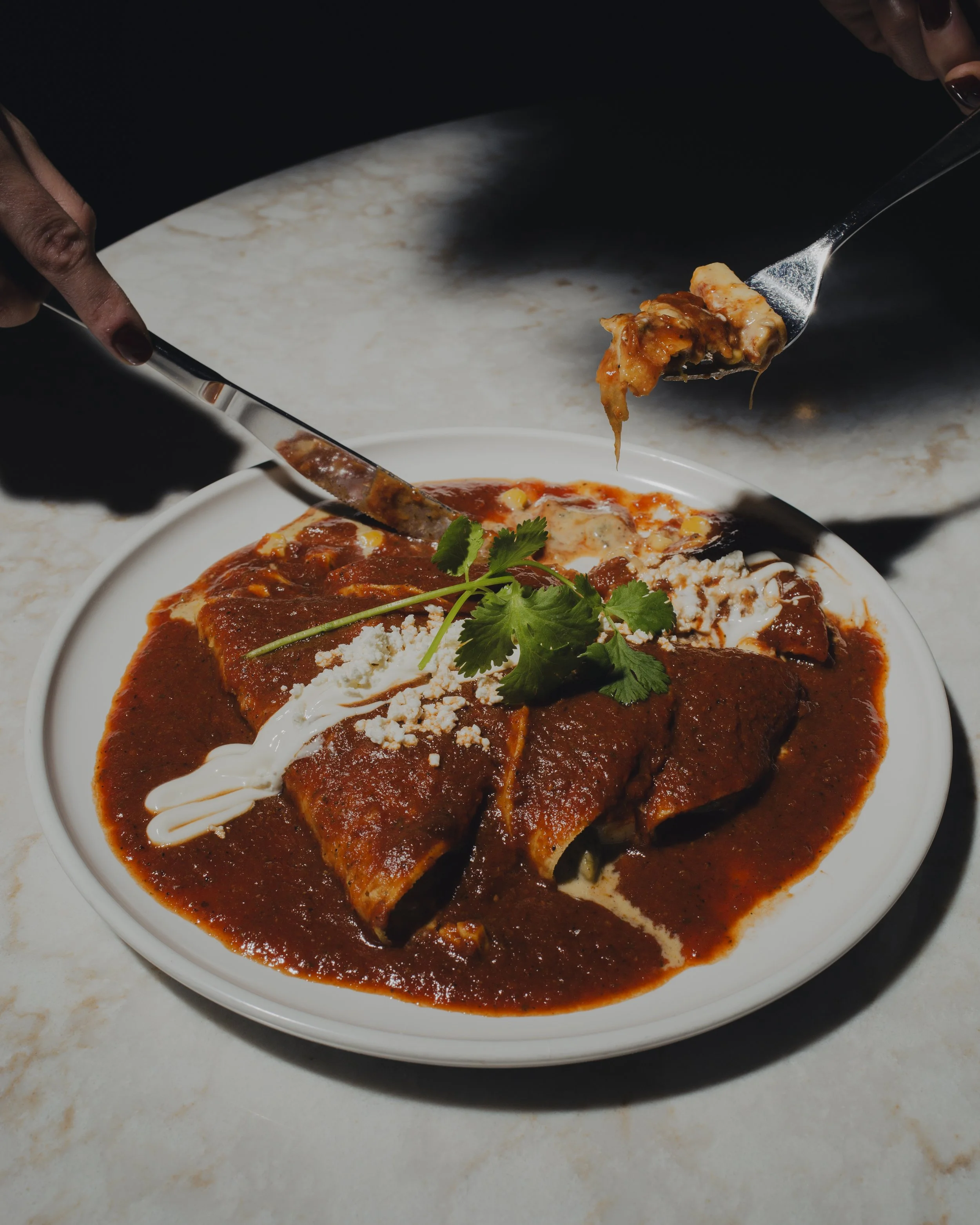 Plate of enchiladas covered with chili sauce, garnished with cilantro, with a drizzle of sour cream and cheese, on a white plate.