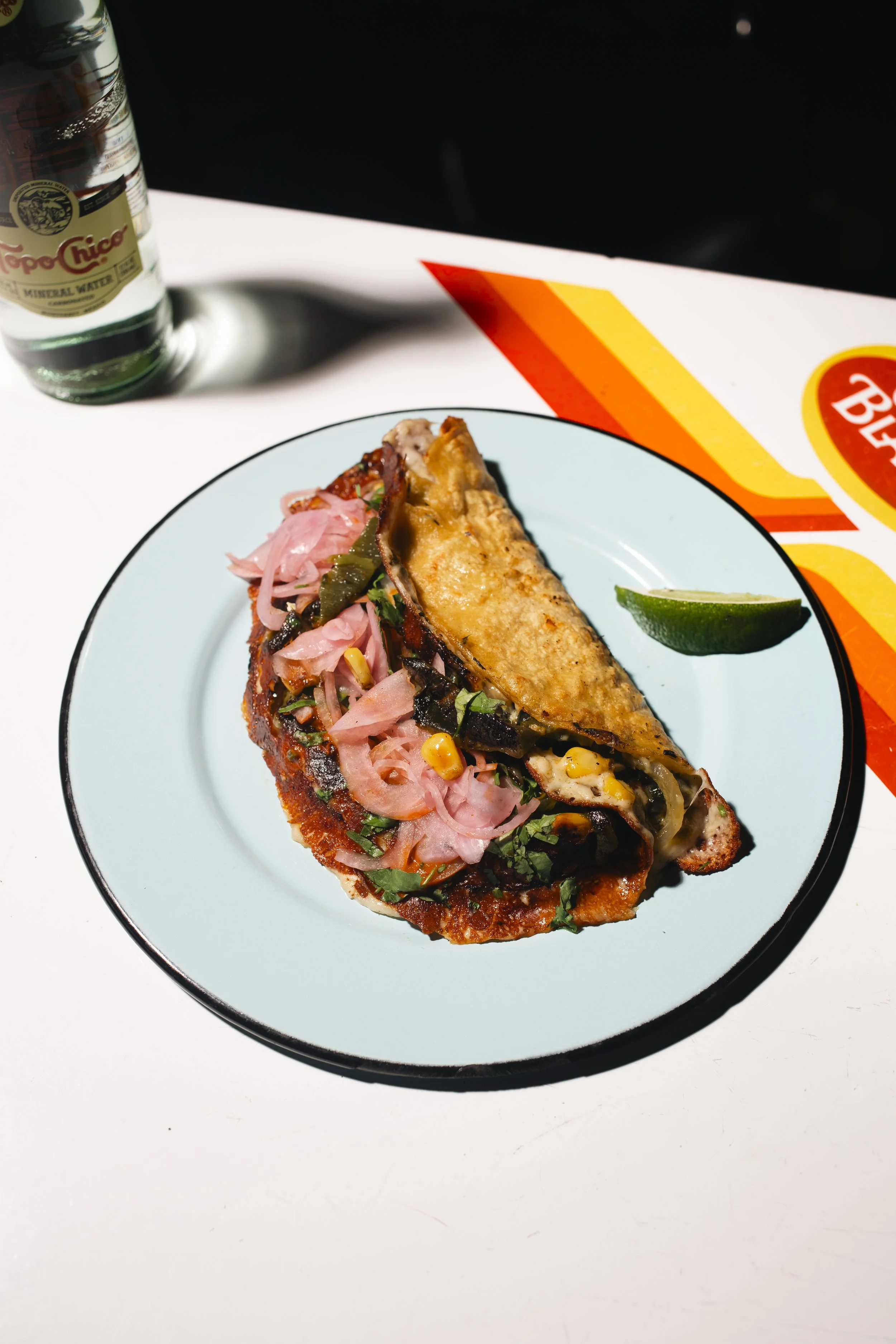 Tacos with pink pickled onions, corn, cilantro, and melted cheese on a white plate, with a lime wedge.