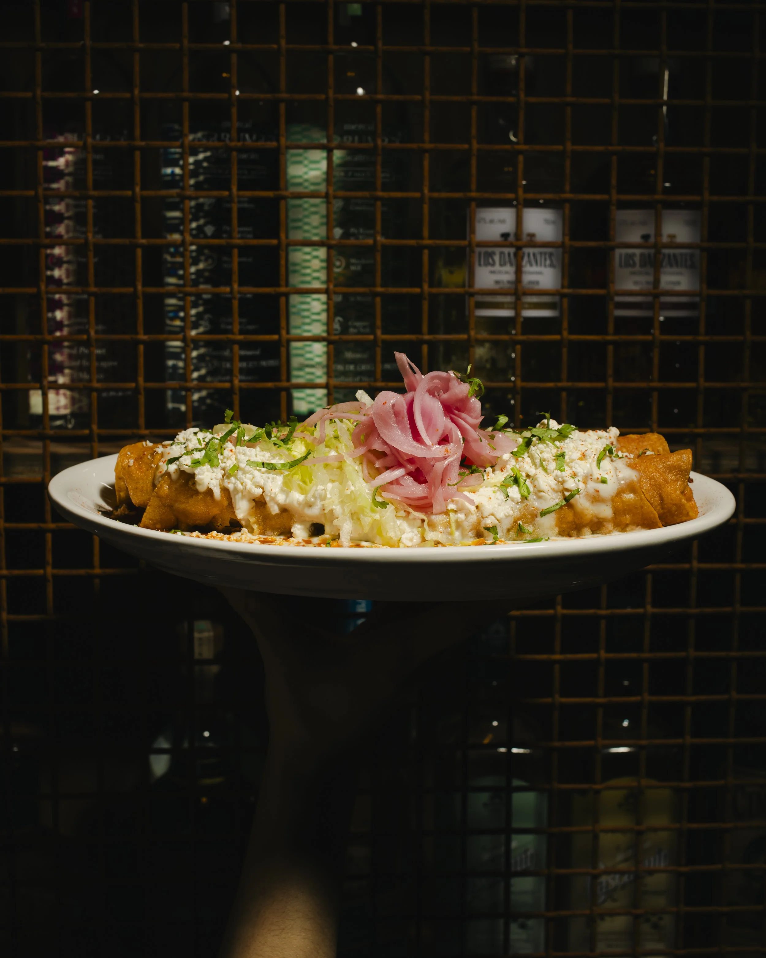 Plate of Mexican food with folded tortillas, shredded lettuce, cheese, pickled onions, and garnishes, against a grid-like background.