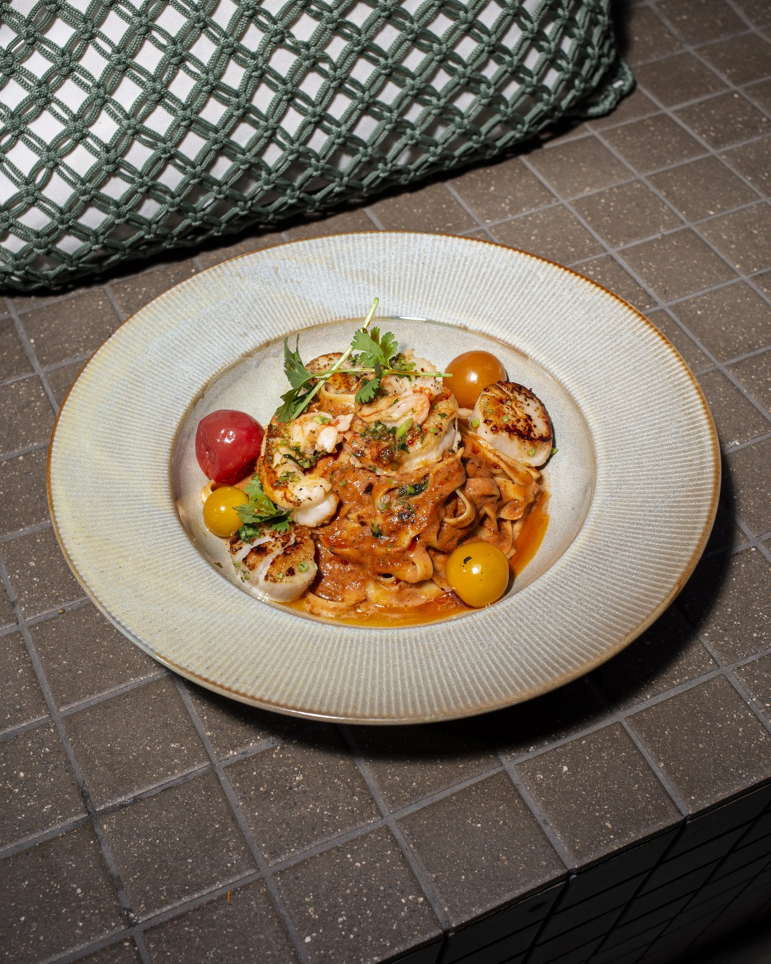 Plate of pasta with tomato sauce, garnished with herbs and cherry tomatoes, served with grilled scallops and garnished with cilantro.