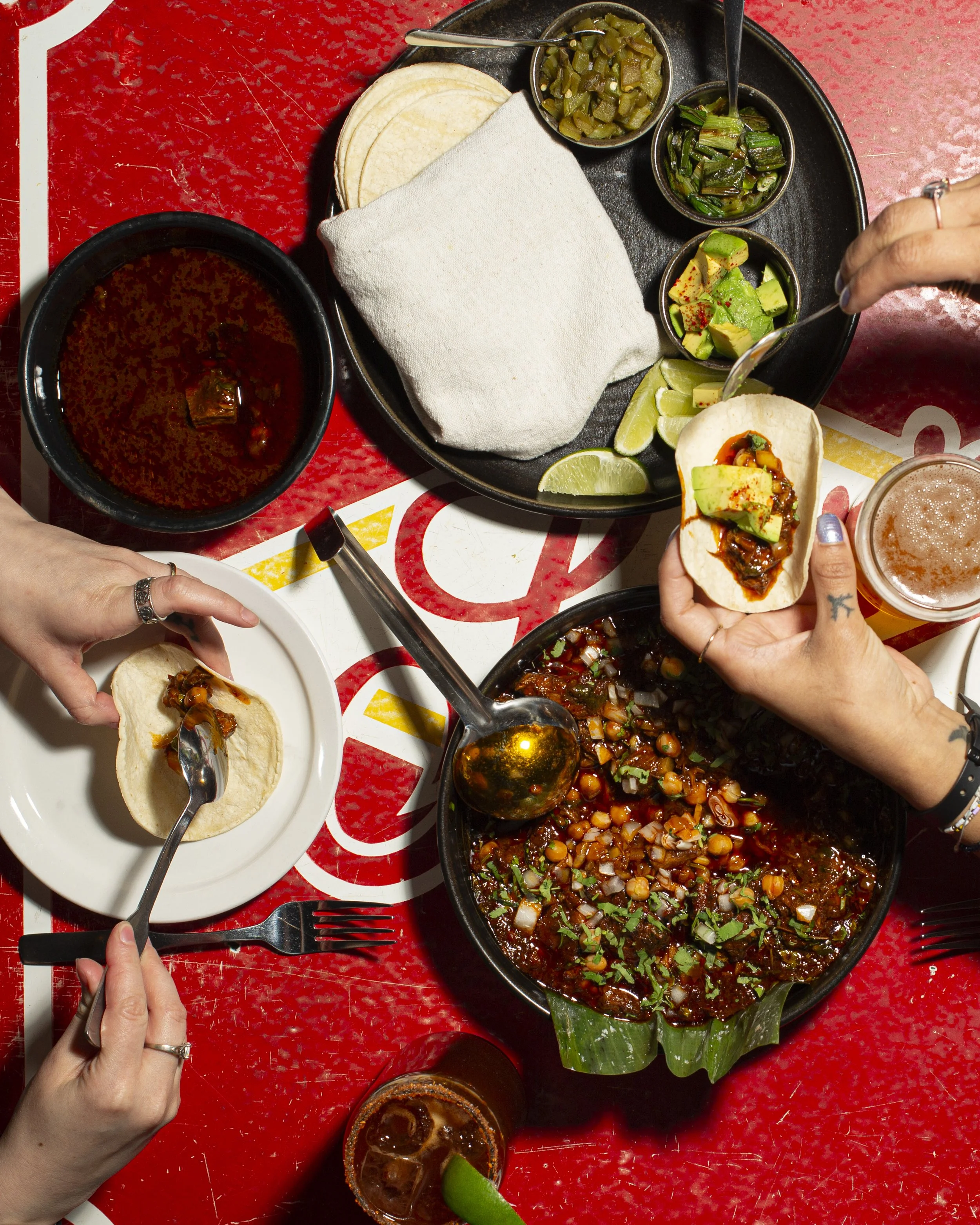 People serving themselves tacos with beans and toppings at a Mexican restaurant.