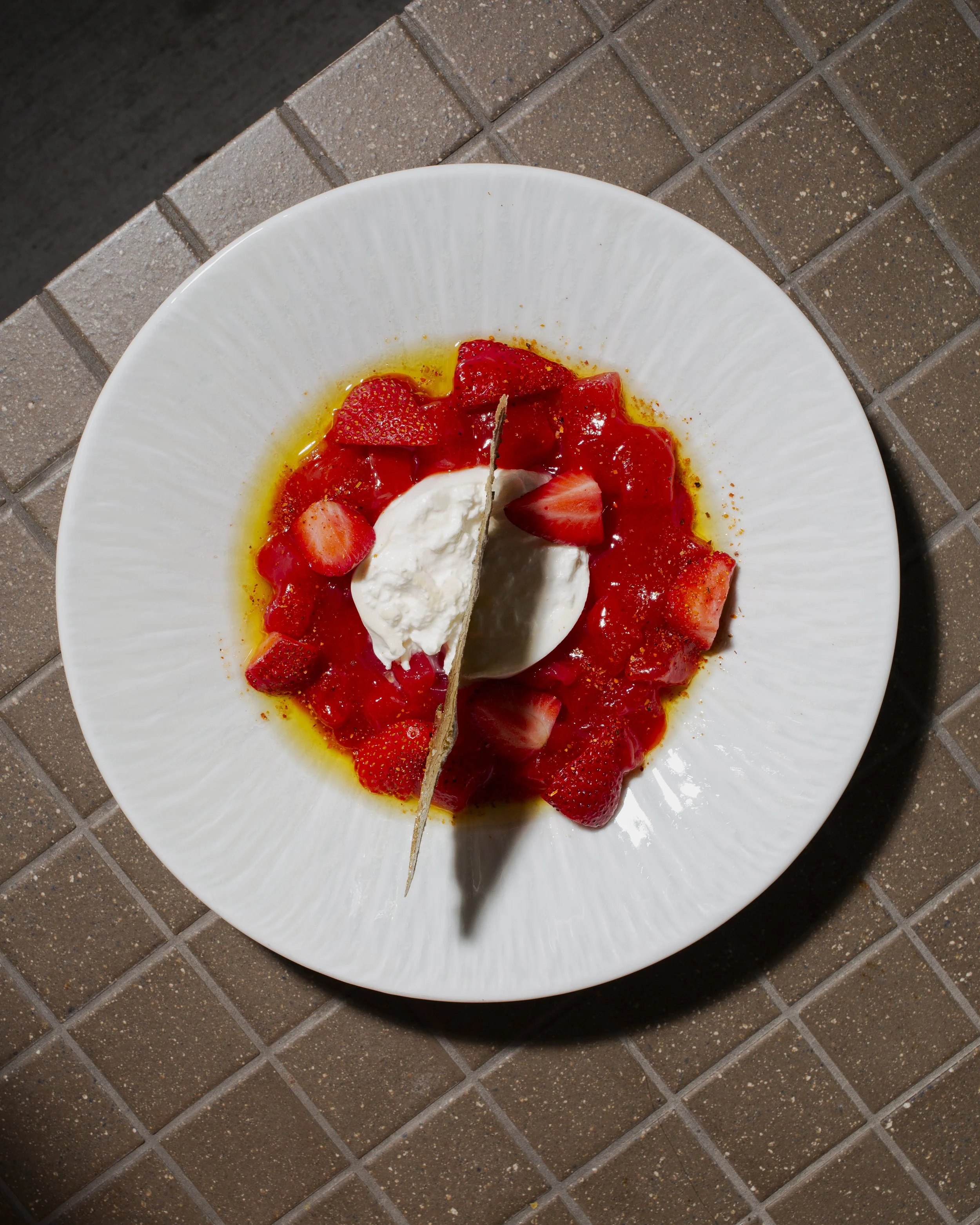 Fresh strawberry dessert with whipped cream on a white plate, with a crispy waffle cookie on top.