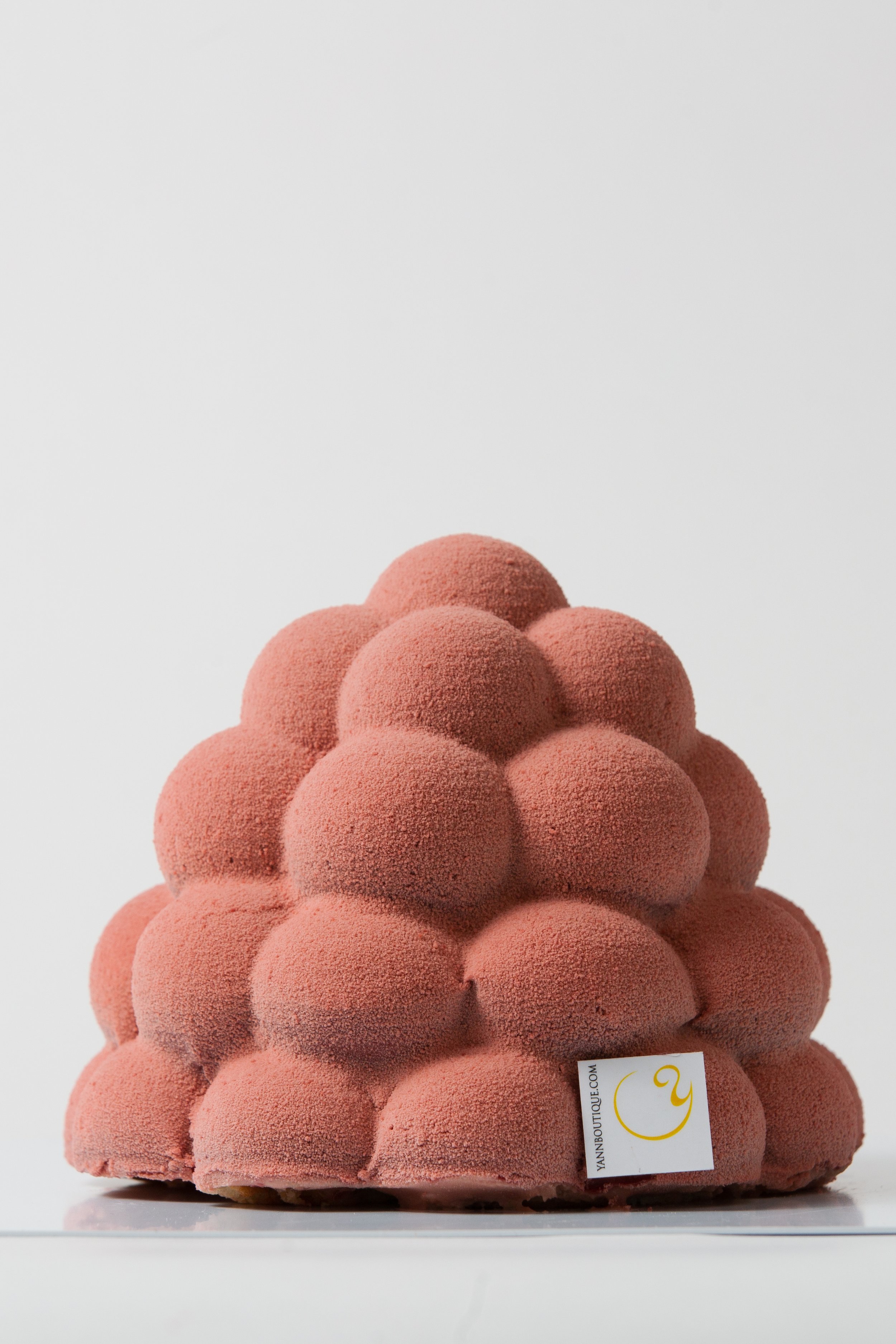 A pink, textured, cone-shaped dessert made of rounded segments, with a tag that reads "yanboutique.com".