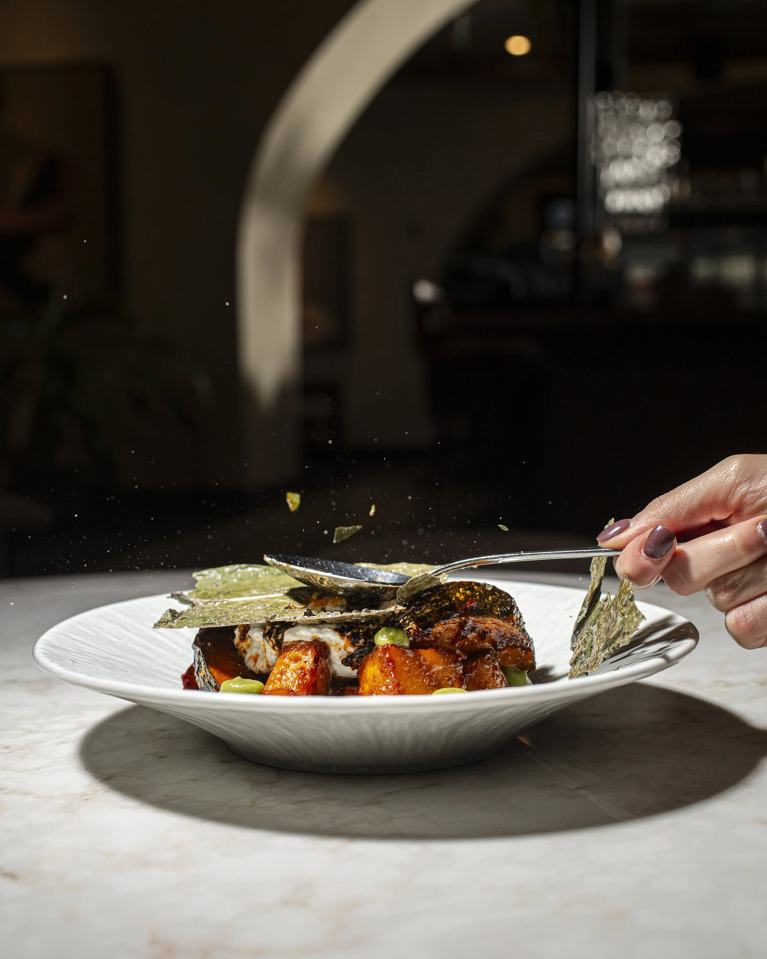 Person sprinkling herbs onto a plated dish of seafood and vegetables.