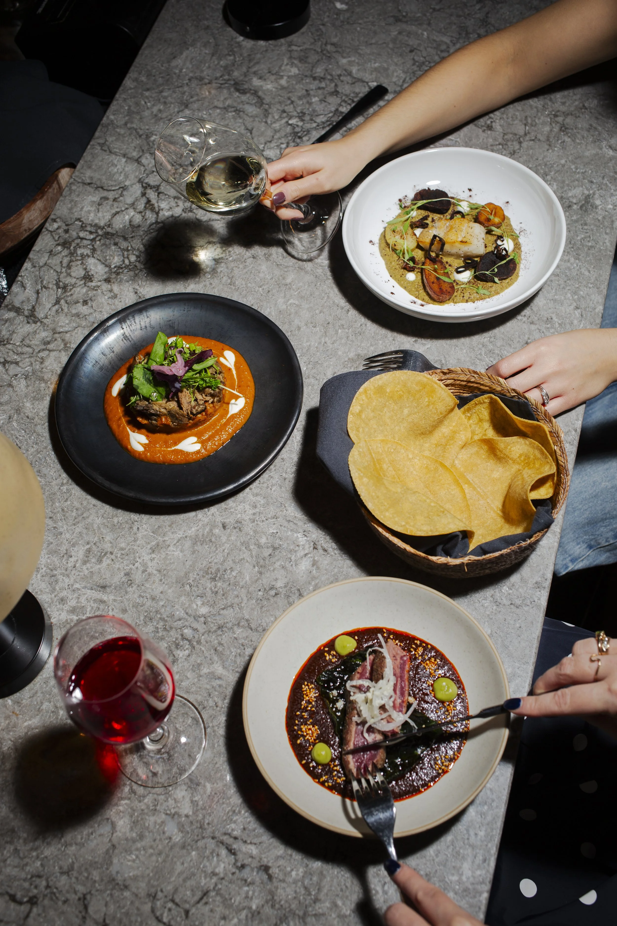 Table with dishes of gourmet food, bread chips, and drinks including white and red wine, in a fine dining setting.