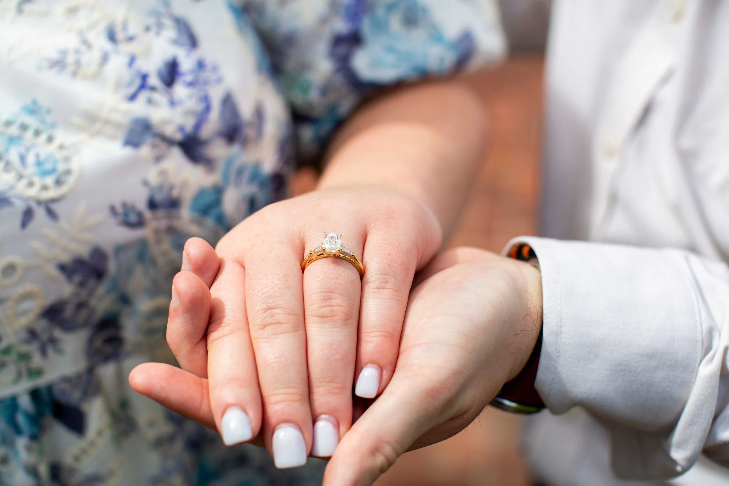A woman rests her hand in a man's hand while showing off her new diamond engagement ring.