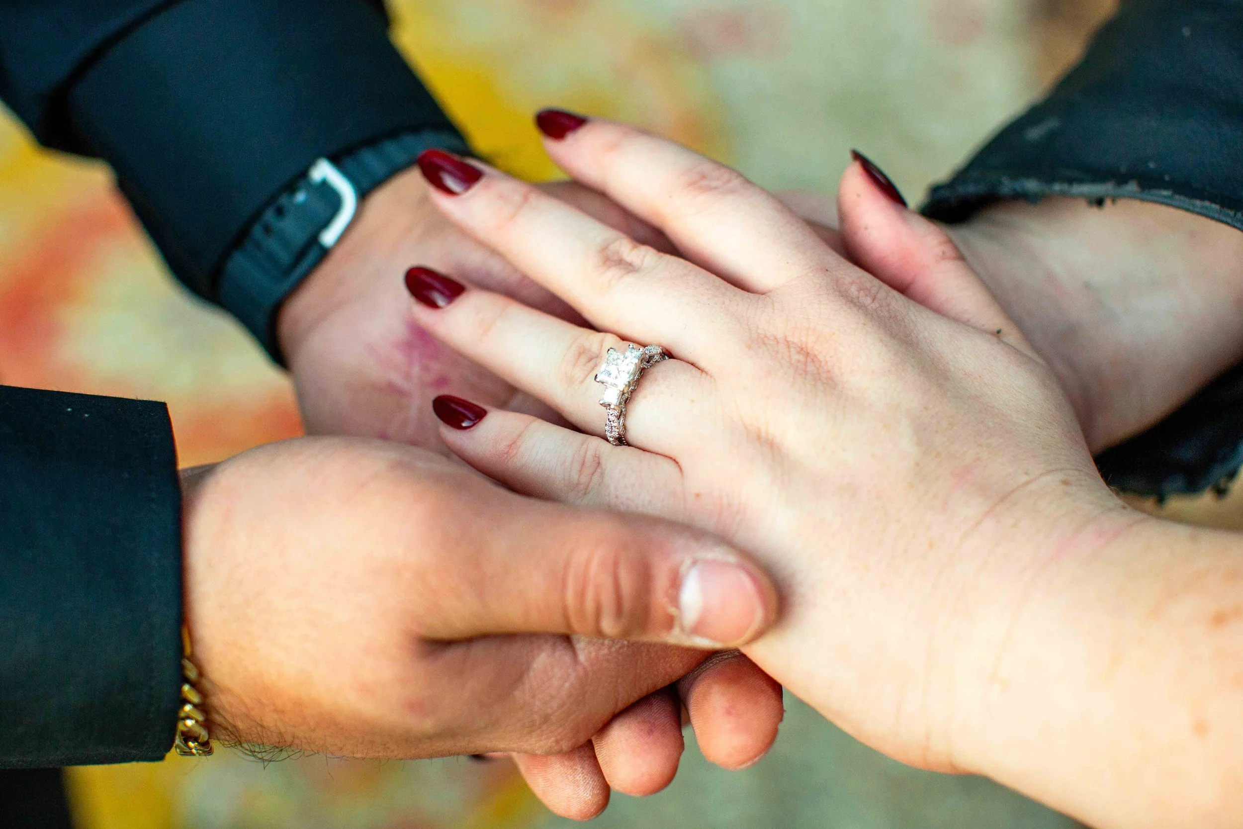 A woman rests her hand in her fiancé's hands to show off her new engagement ring.