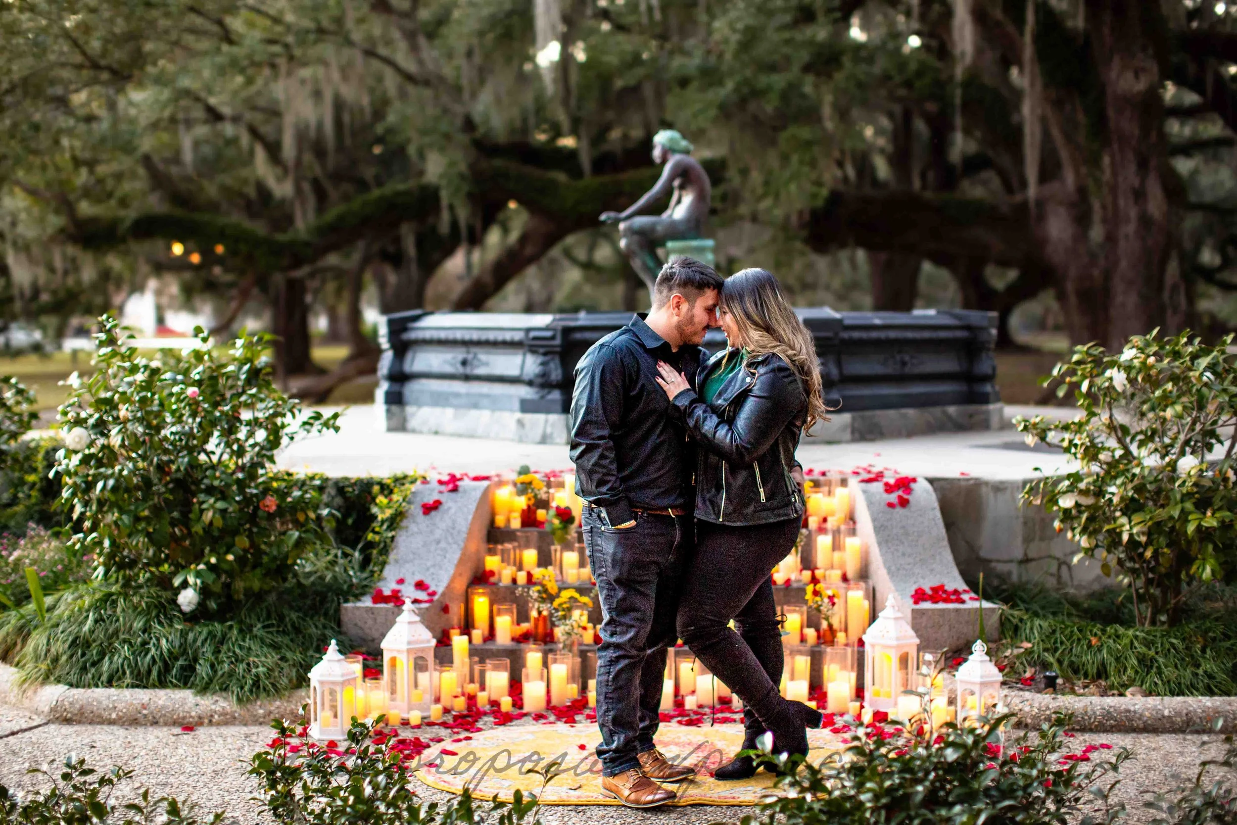 A man and a woman pose in front of a romantic display arranged on the steps of a stone fountain following their engagement in New Orleans City Park.