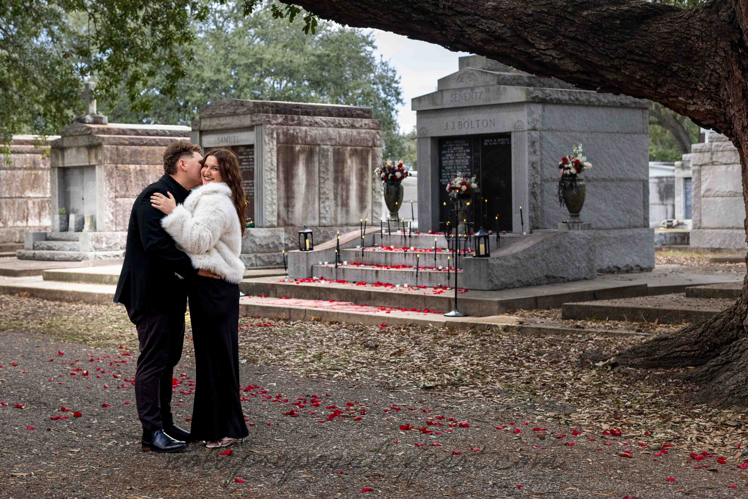 A man whispers in his fiance's ear while they stand in front of a mausoleum decorated for a romantic surprise proposal in a New Orleans cemetery.