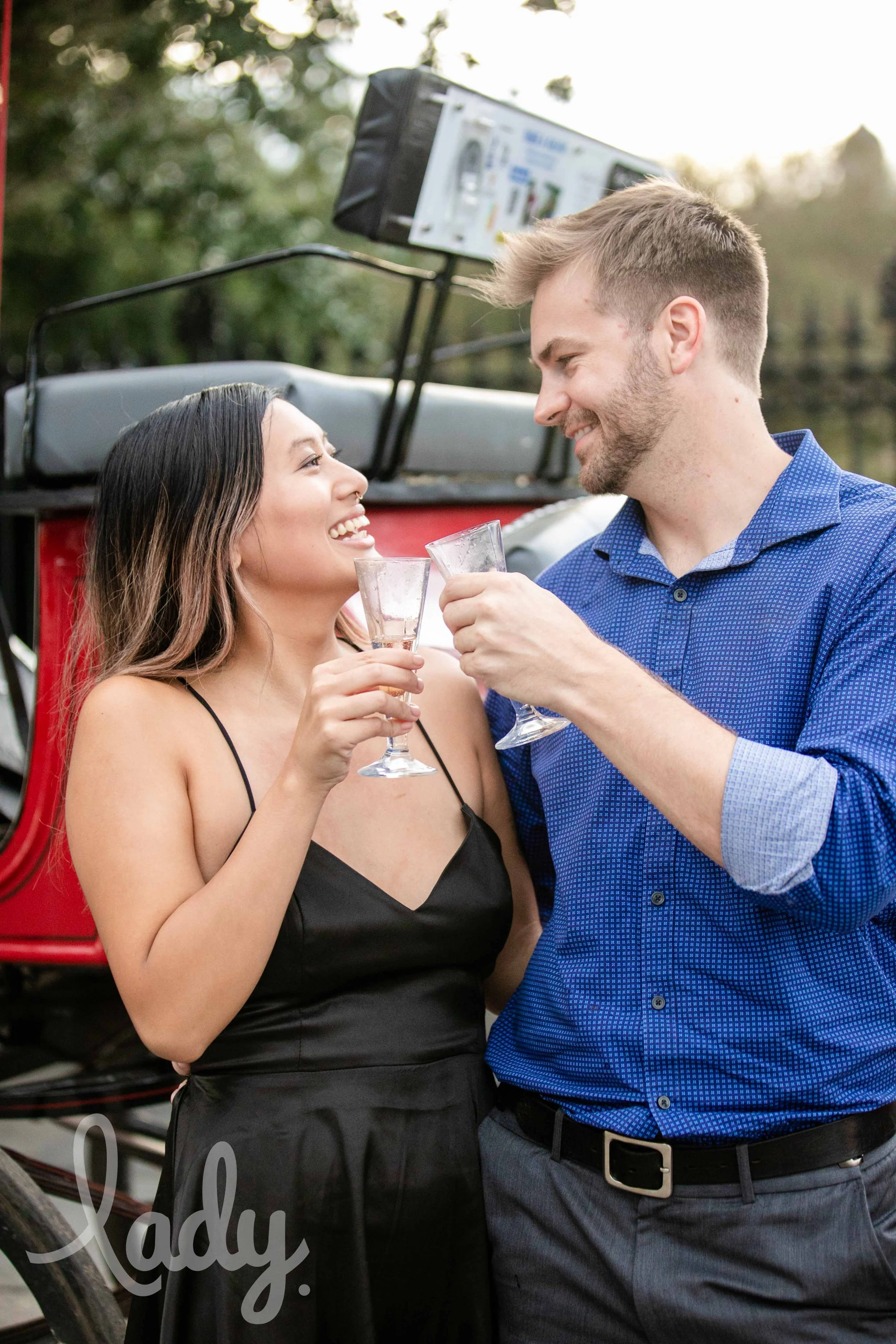 A newly engaged couple toasts in front of a horse-drawn carriage.