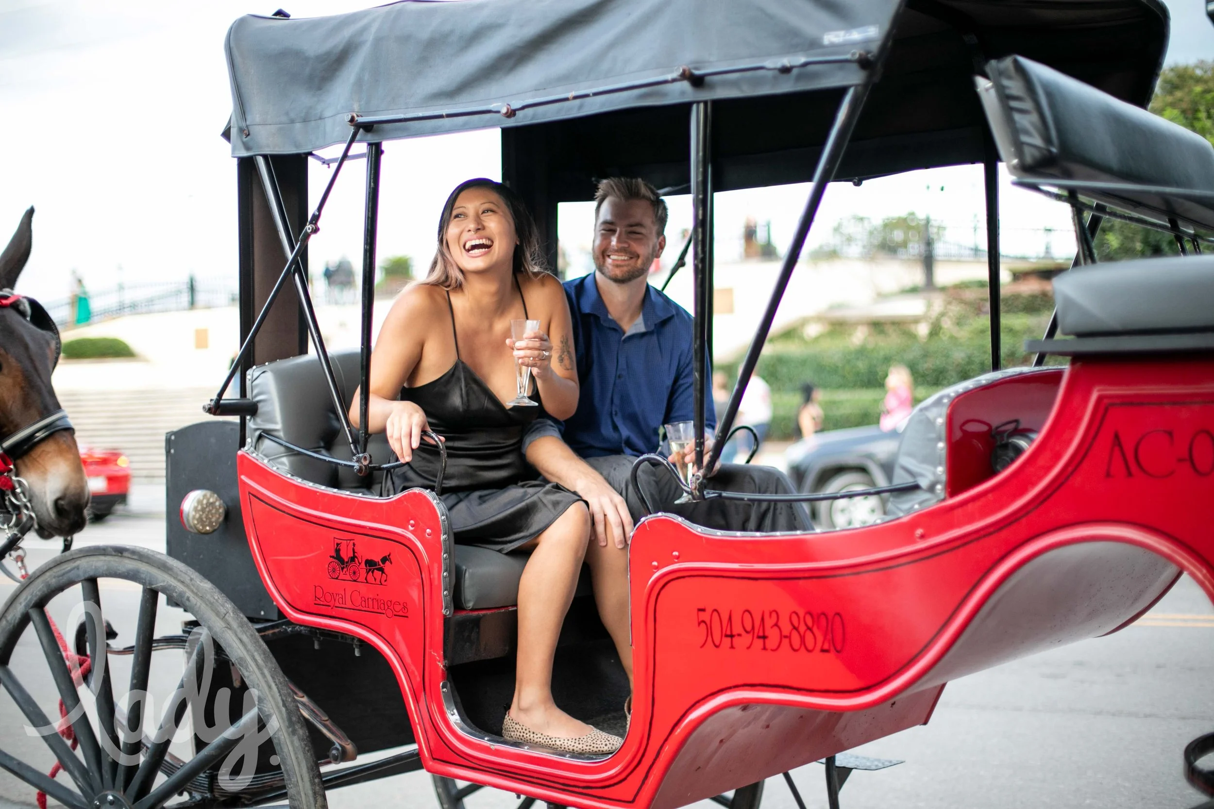 a newly engaged couple laughs while riding in a horse-drawn carriage.