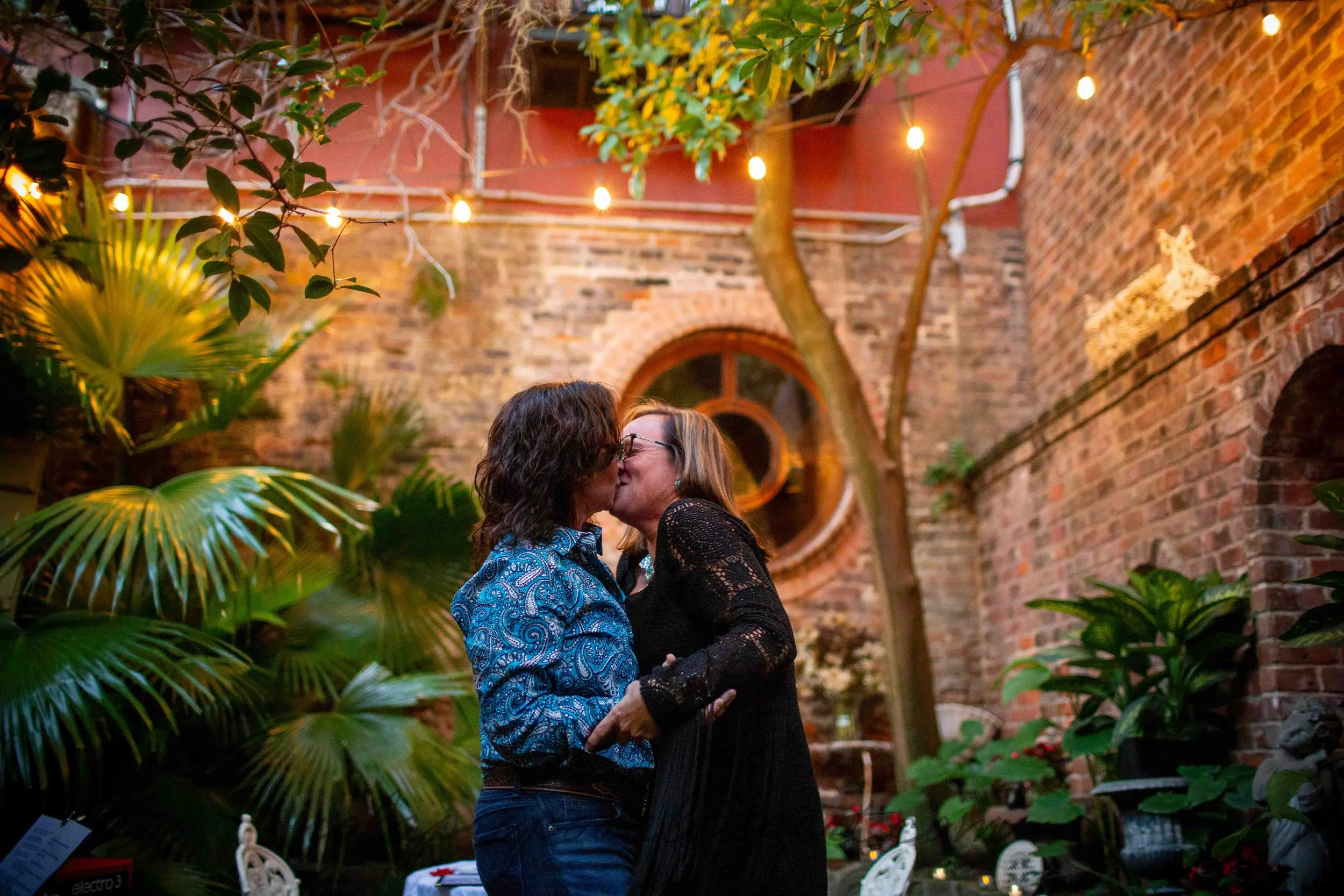 A lesbian couple embraces with a happy kiss inside a French Quarter courtyard following their surprise marriage proposal.