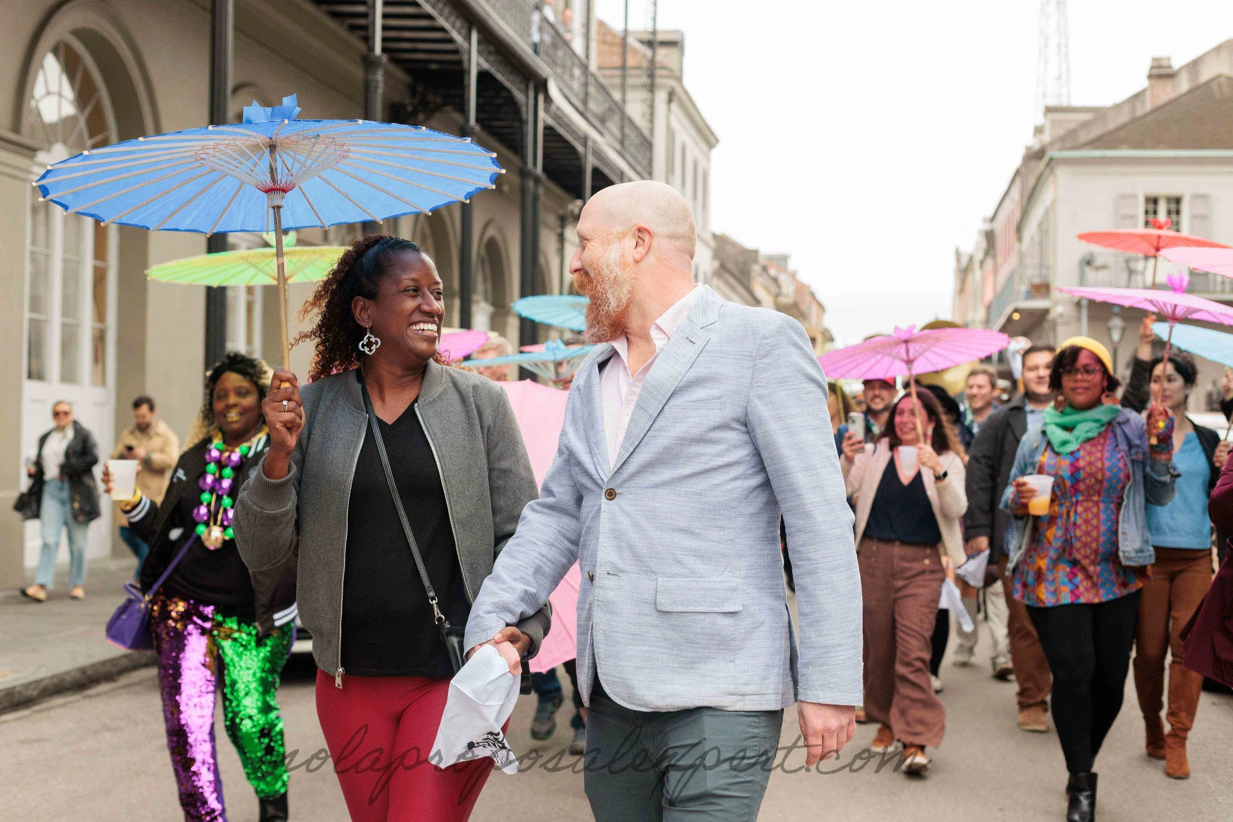 a couple walks in front of a second line parade in the french quarter after their mardi gras surprise proposal in new orleans.