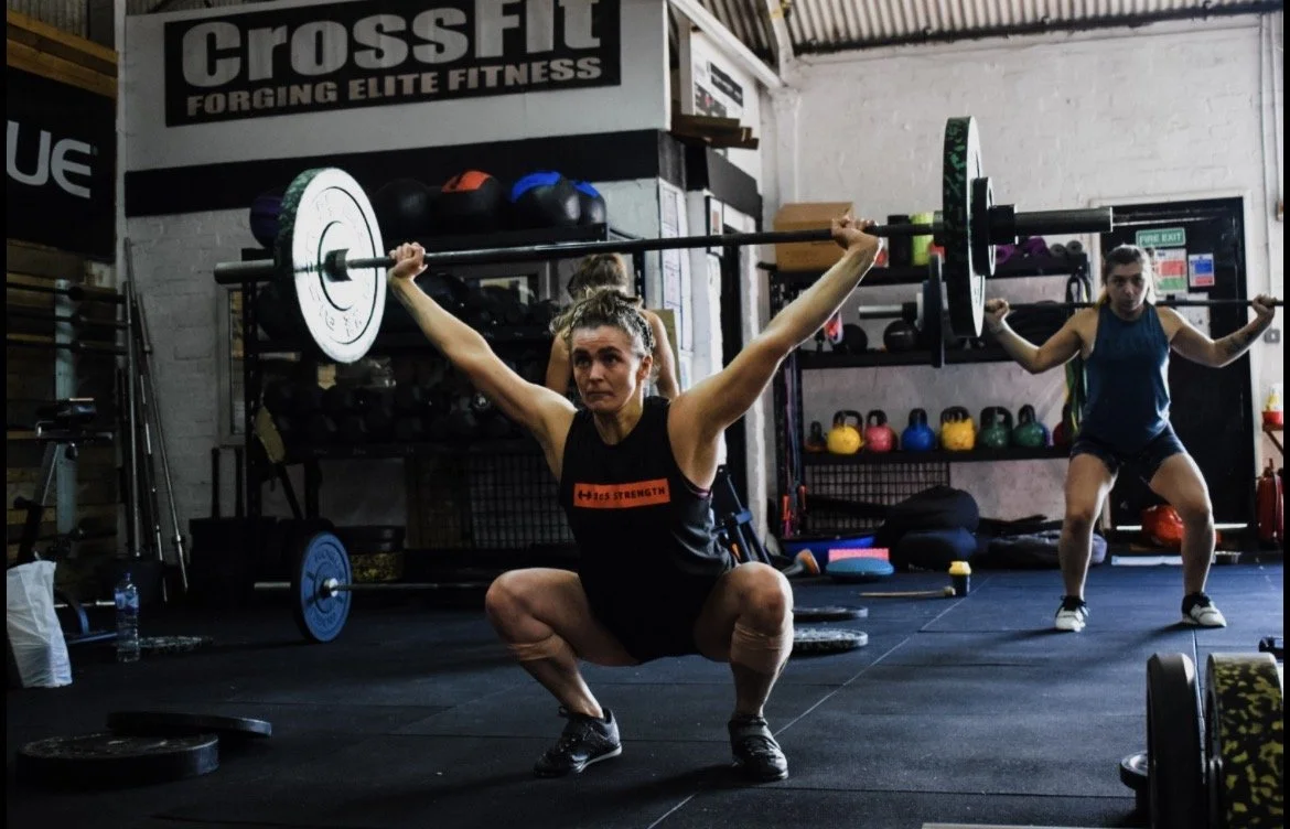 image of two female athletes performing olympic lifts - the Snatch with one athlete at the bottom of the snatch in overhead squat position.
