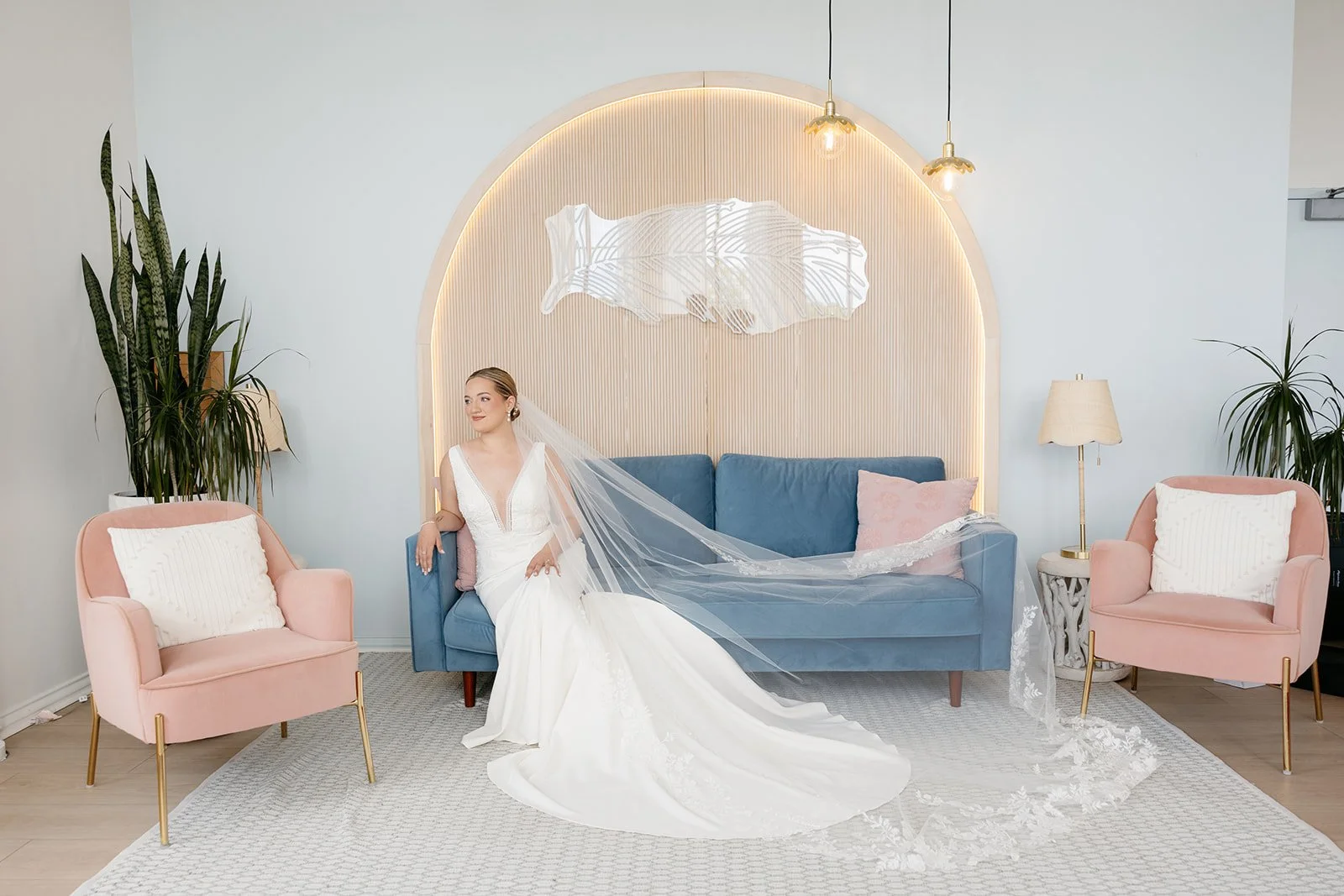 Arbor at the Port bride posing in a modern bridal lounge with blue velvet sofa, soft pink chairs, and elegant wedding veil in Rochester, NY.