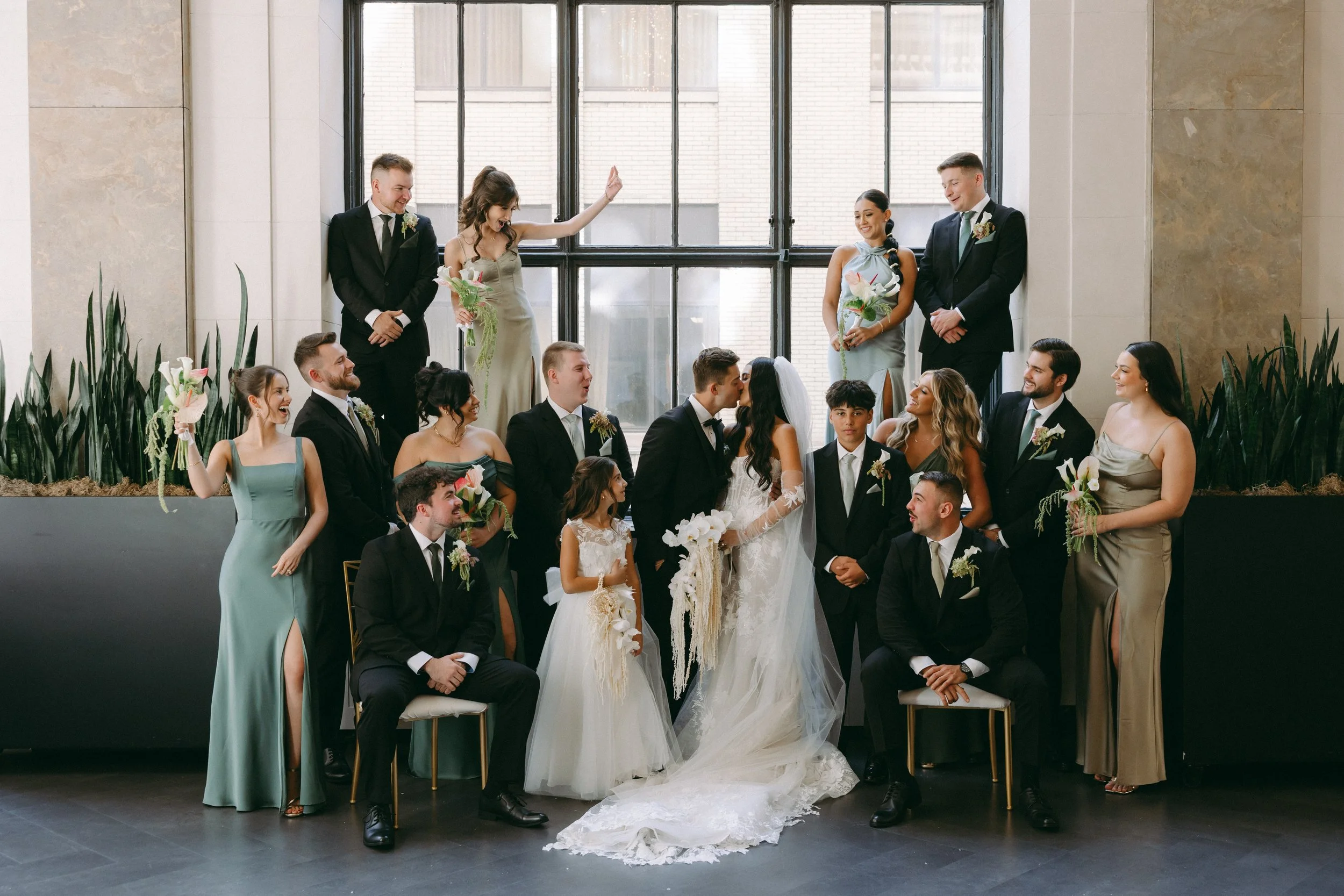 Arbor Midtown wedding party portrait in a bright modern venue with large windows, greenery, and bridesmaids and groomsmen celebrating in Rochester, NY.