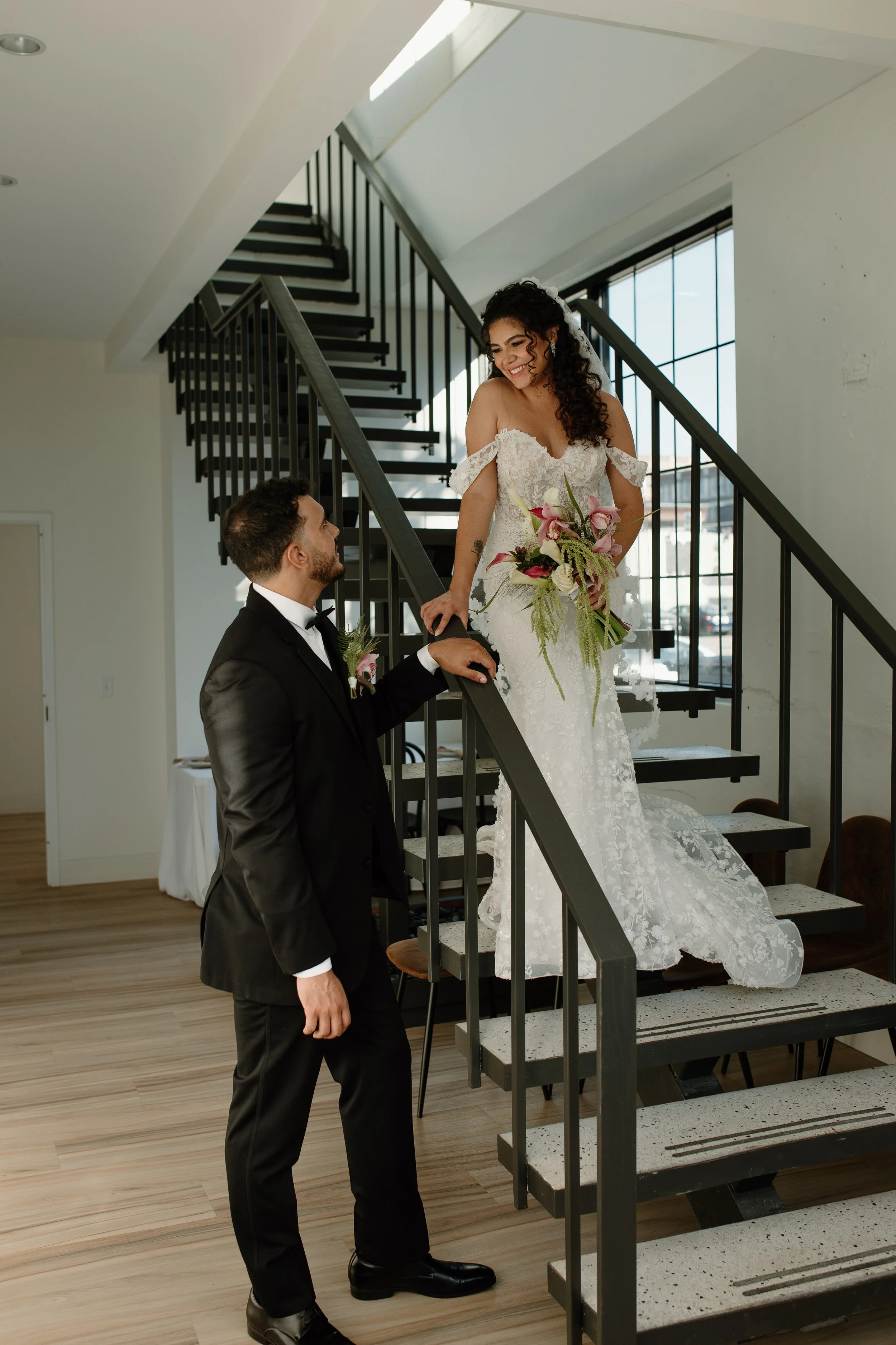 Bride and groom sharing a romantic moment on the staircase inside Arbor Loft wedding venue with modern industrial windows and natural light.
