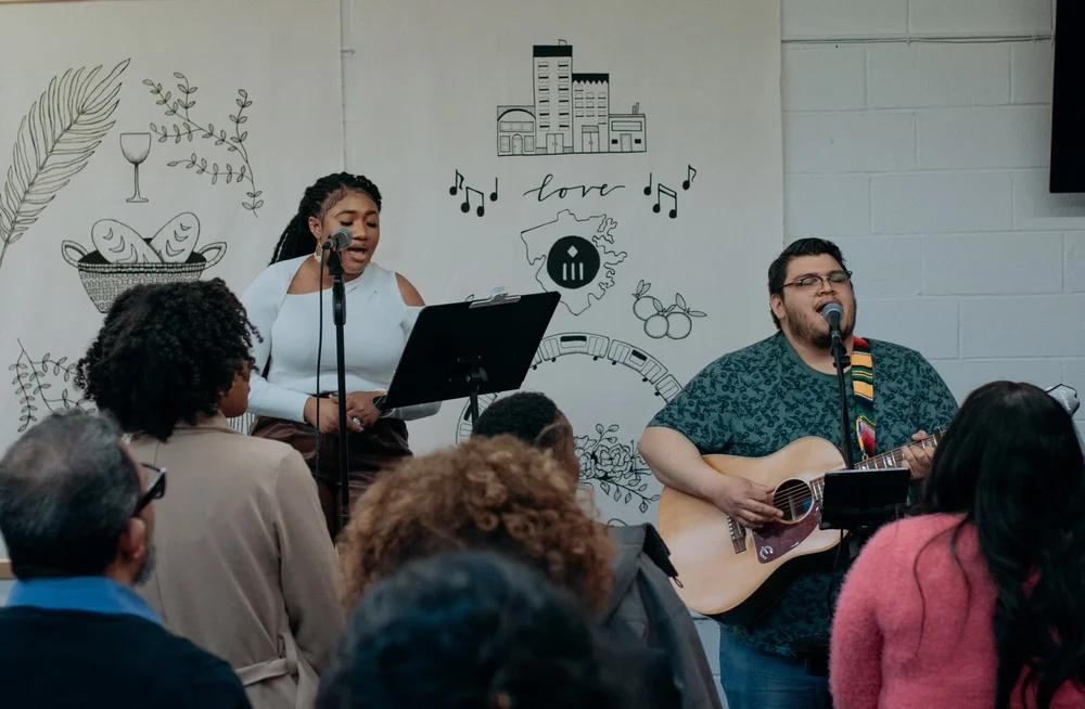 Worship leaders singing in front of the congregation, beside the church mural