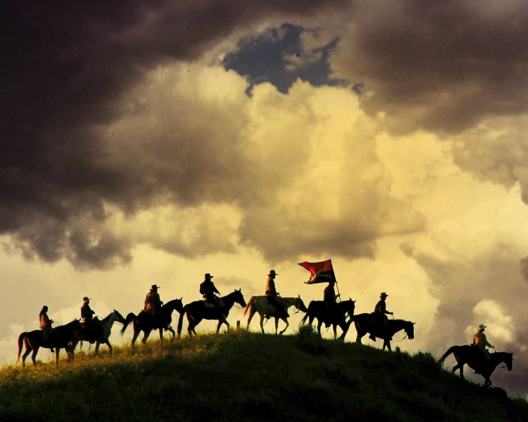 Silhouetted cowboys ride along a ridge beneath dramatic storm clouds, part of the visual research for Cowboys and Cancer.