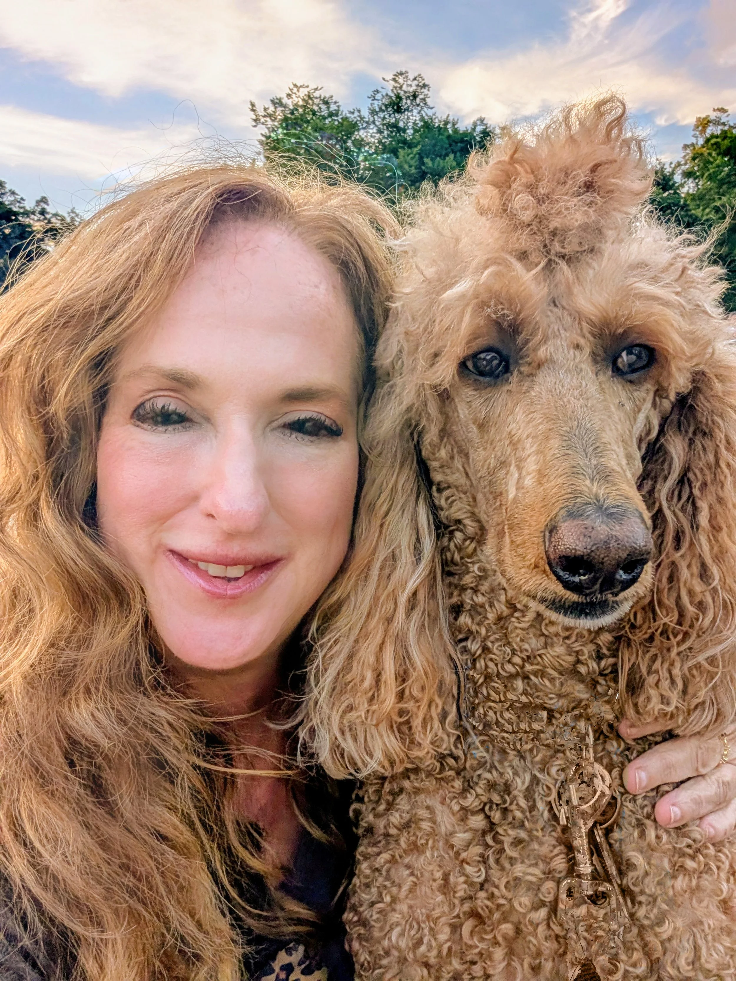 KatMoon Landes poses closely with Bernie, her standard poodle, in a warm outdoor portrait.