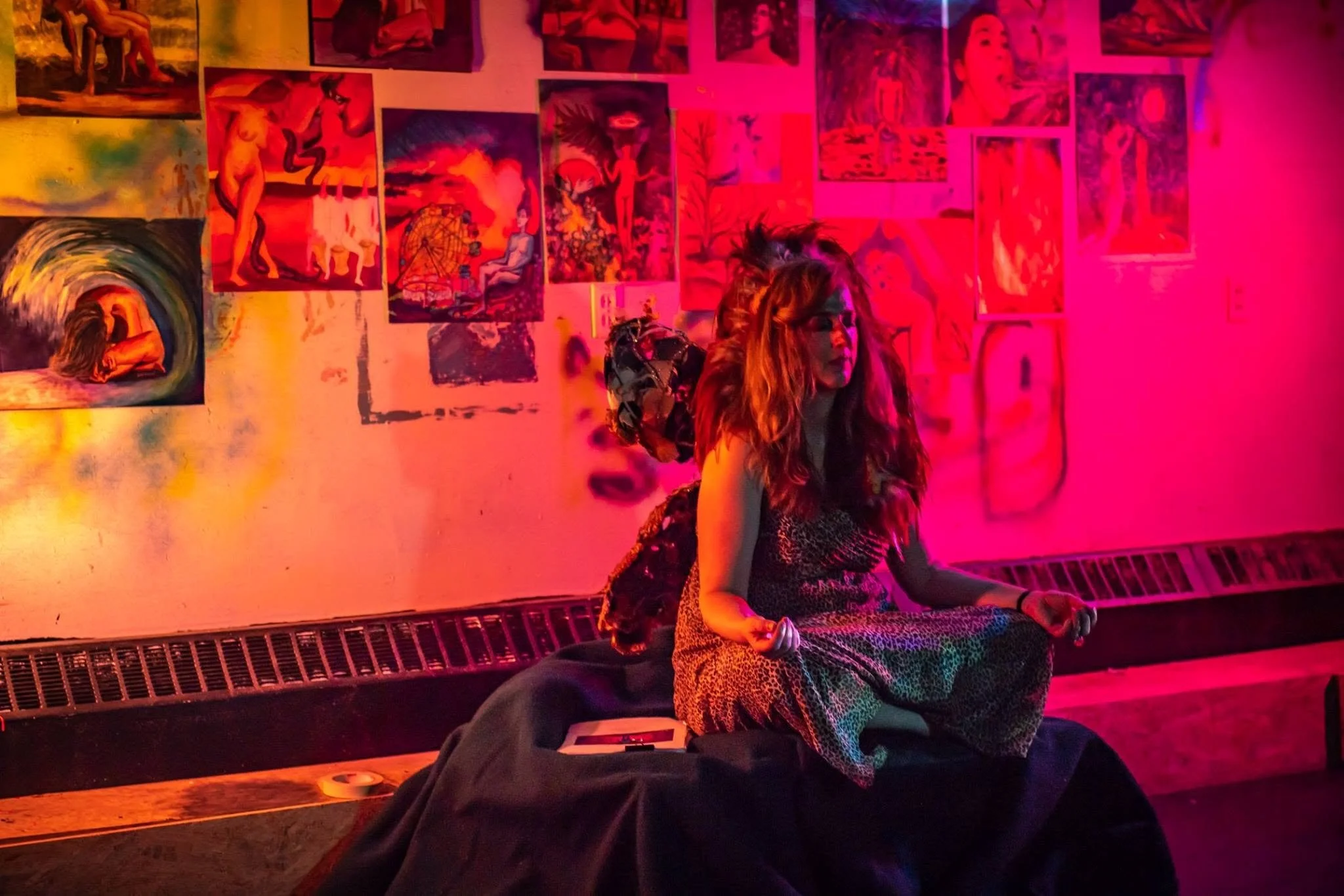 A performer sits beneath vivid red and pink projections from The Broken Hallelujah, surrounded by layered drawings and projected imagery in an immersive installation.