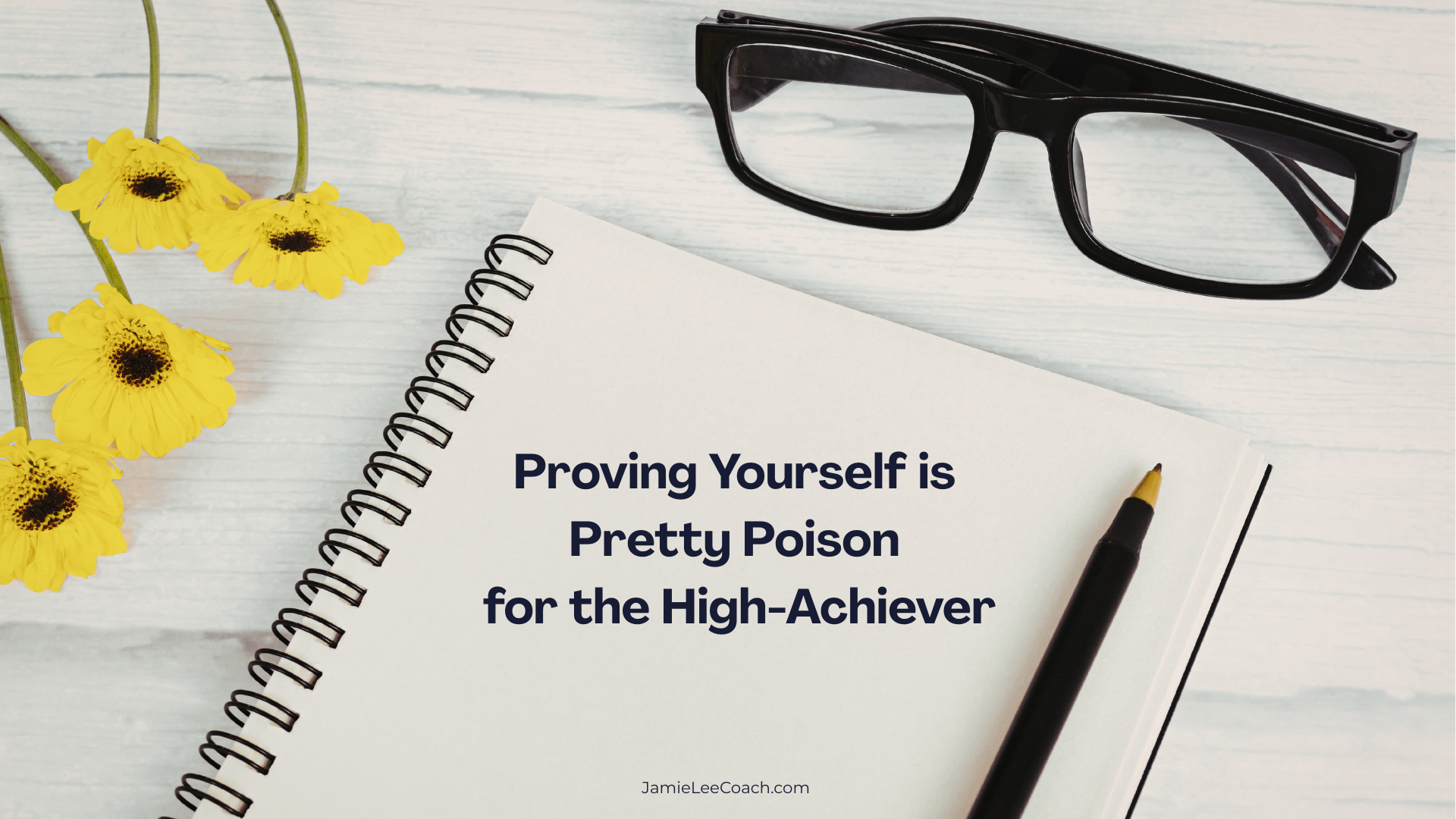 Top-down shot of a minimalist workspace on a light wood surface featuring a spiral notebook, a pair of black-rimmed glasses, a black pen, and three bright yellow flowers. Centered on the notebook page is the text: "Proving Yourself is Pretty Poison"