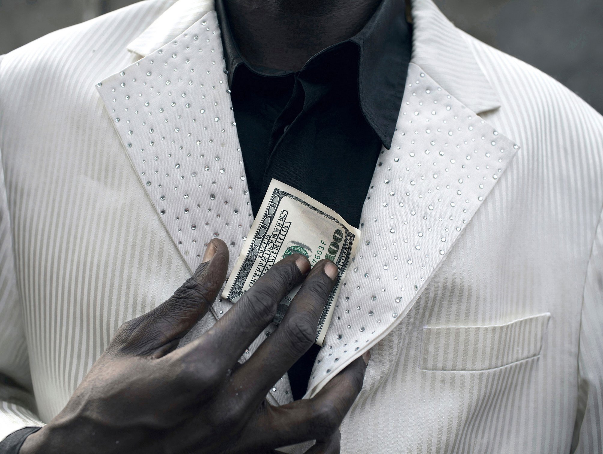  KINSHASA, DEMOCRATIC REPUBLIC OF CONGO - FEBRUARY 12: Jika, a senior Sapeur shows a USA one hundred dollar bill while wearing his white diamond suit close to his home in the Mombele area on February 12, 2012 in Kinshasa, DRC. Jika loves Japanese fas