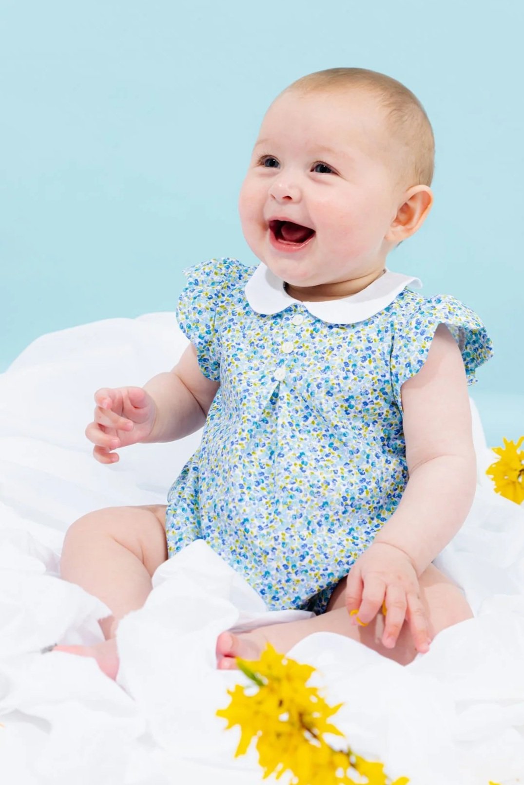 Pagliaccetto neonata a fiori blu e verdi con colletto in lino bianco e alette a petalo indossato sorriso