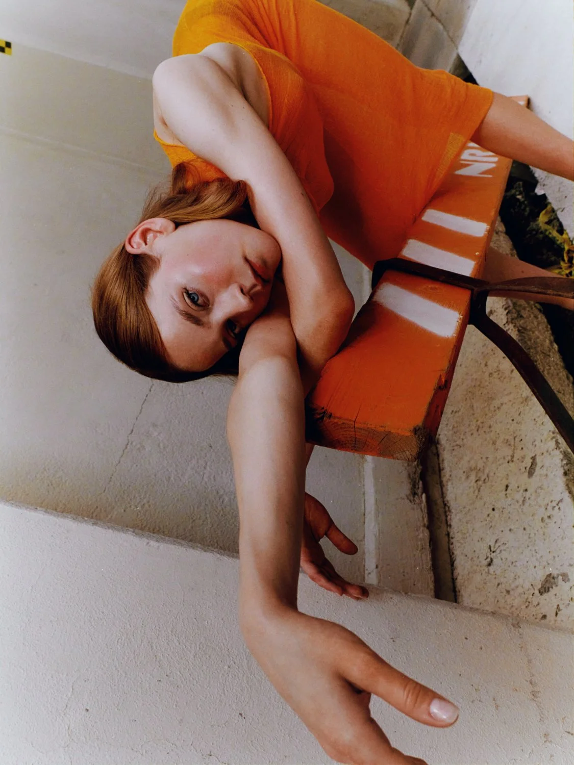 Person in orange dress leaning against orange-striped bench, arm extended.