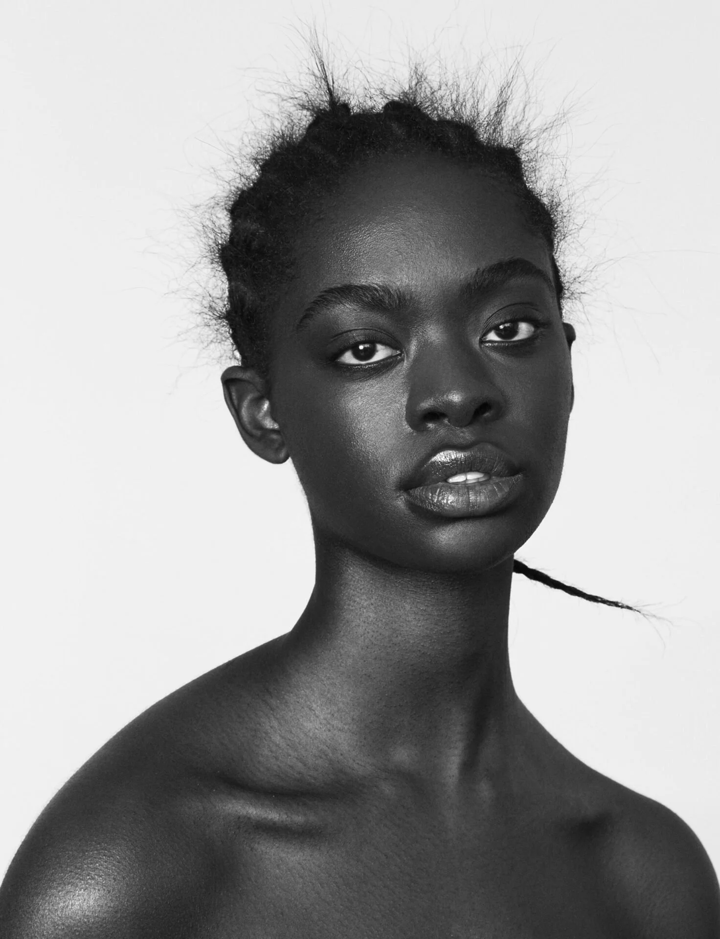 Black and white portrait of a person with braided hair, facing forward, on a plain background.