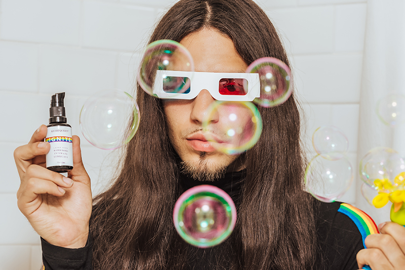 Model wearing 3D blue & red glasses pictured infront of white bathroom tile with bubbles floating around. 