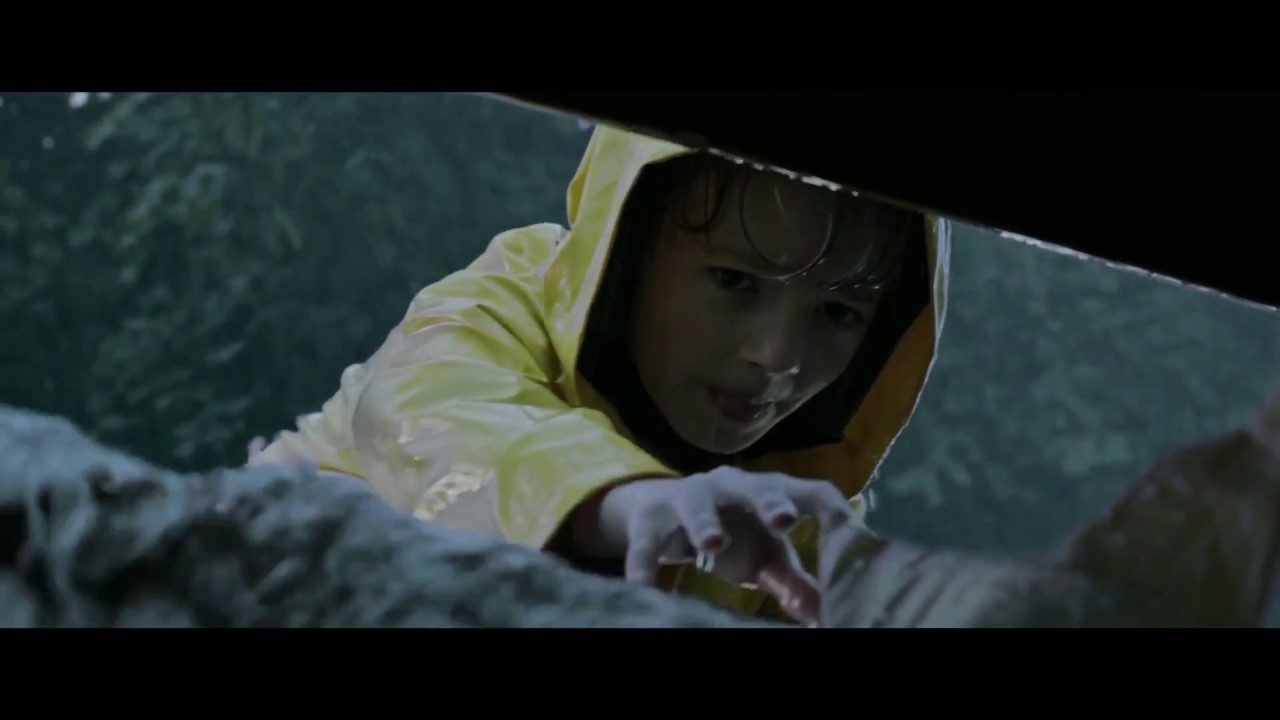 Jackson Robert Scott, as Georgie Denbrough, reaches into the sewer to retrieve his paper boat from Pennywise the Dancing Clown in It