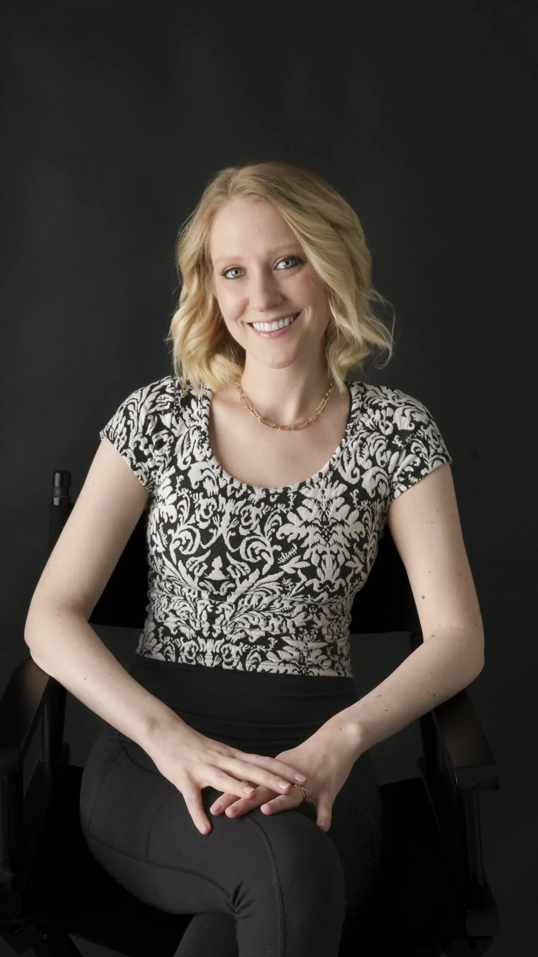 Erika smiling in a black and white outfit with a black backdrop.