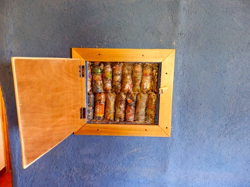 A panel in the interior wall of the house, revealing what the walls are made of — ecobricks made from recycled soda bottles.