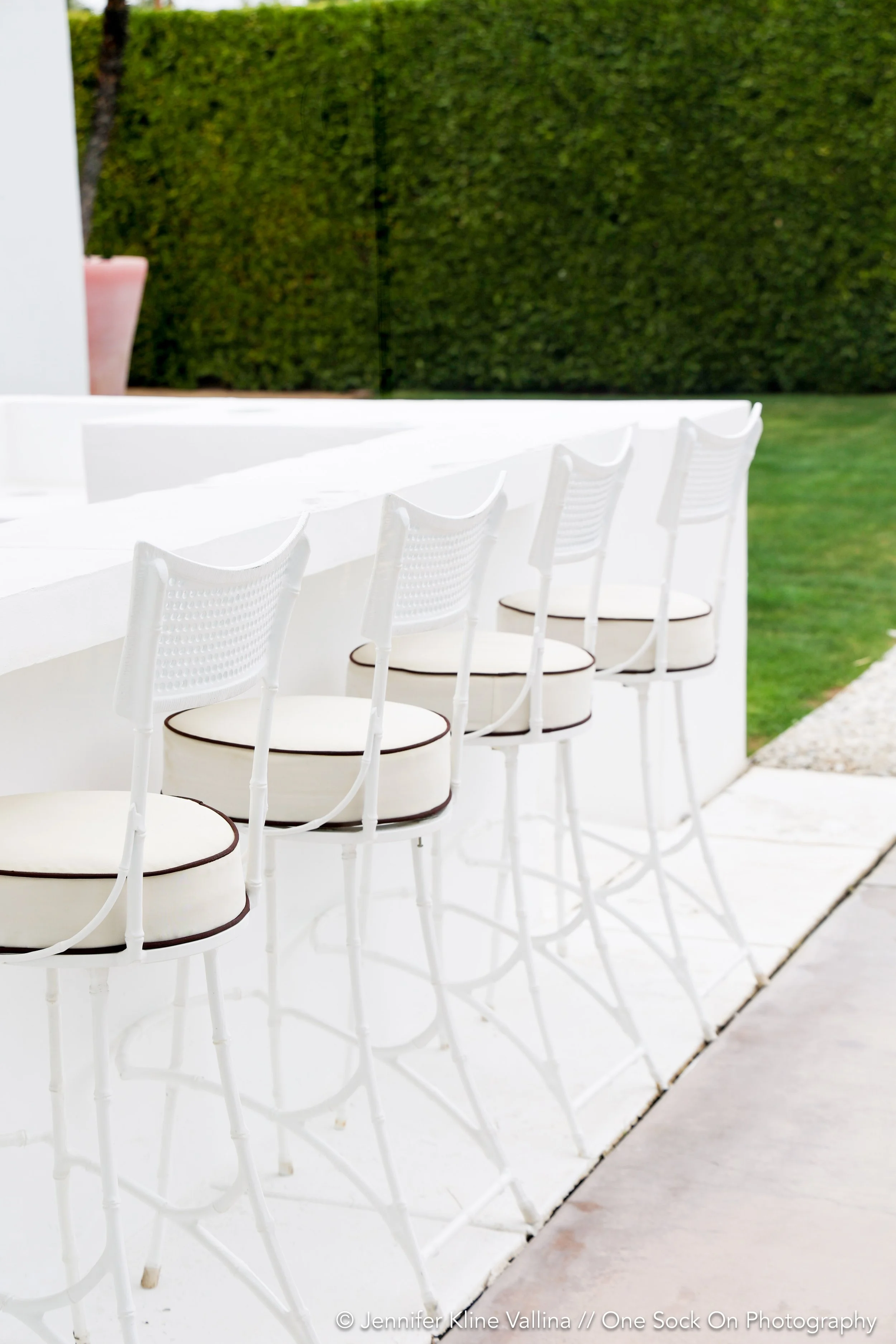 bar stools outdoor grill green hedges with a pop of a pink pillow in background