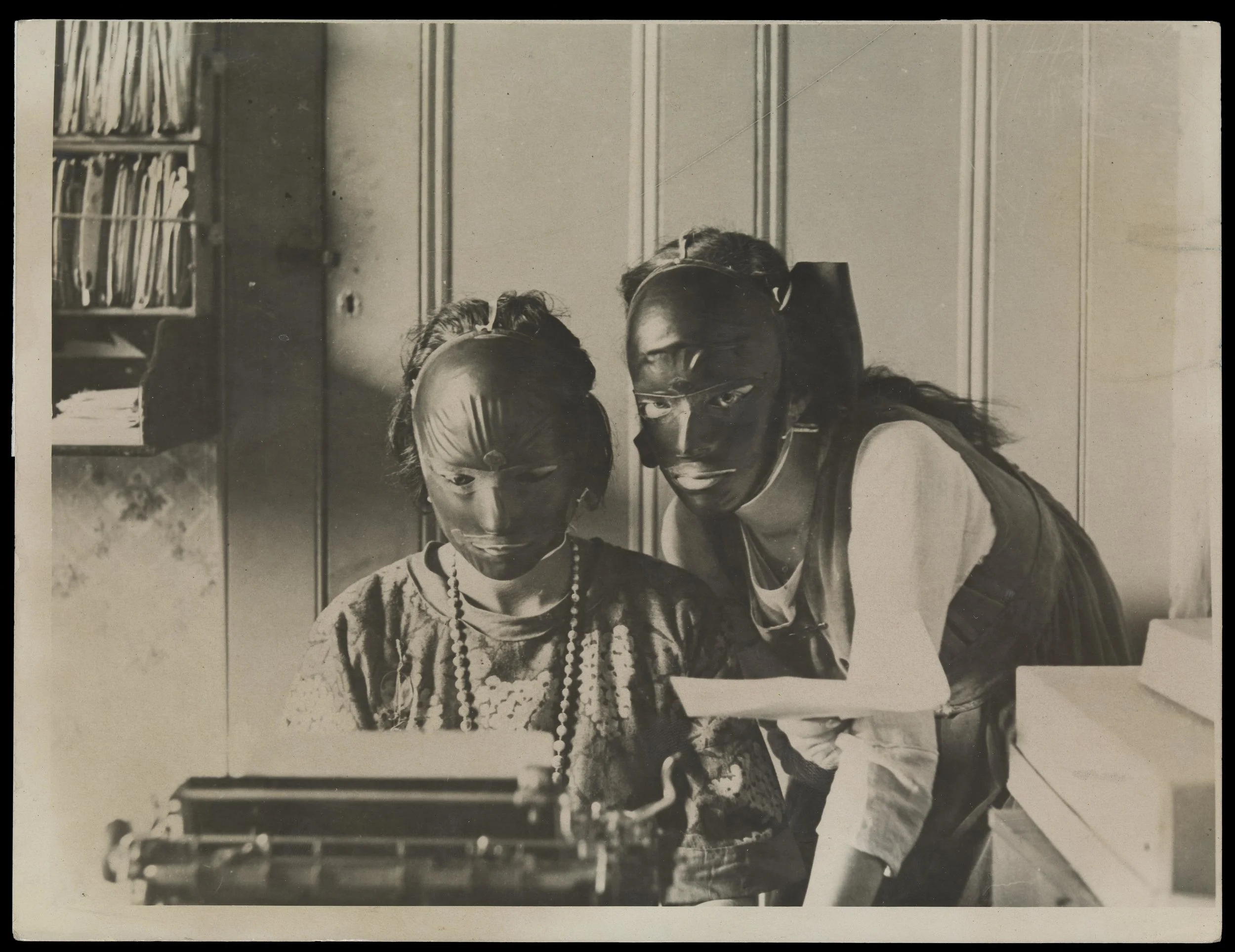 Rubber beauty masks, worn to remove wrinkles and blemishes; modelled by two women at a typewriter (1921)