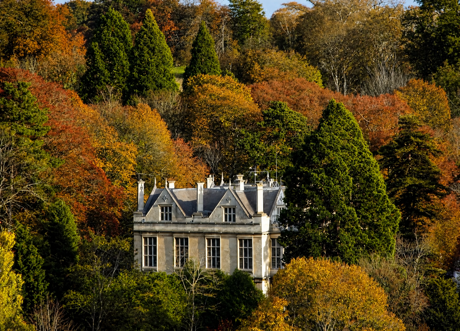 A stone house surrounded by colorful fall foliage, including green, orange, and yellow trees.
