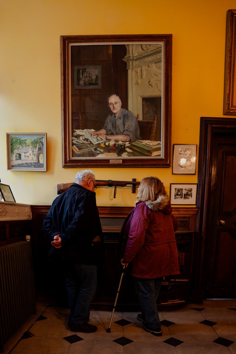 Close-up of a decorative wall panel with ornate scrollwork and the letters 'JH' in the center, with stained glass windows in the background.
