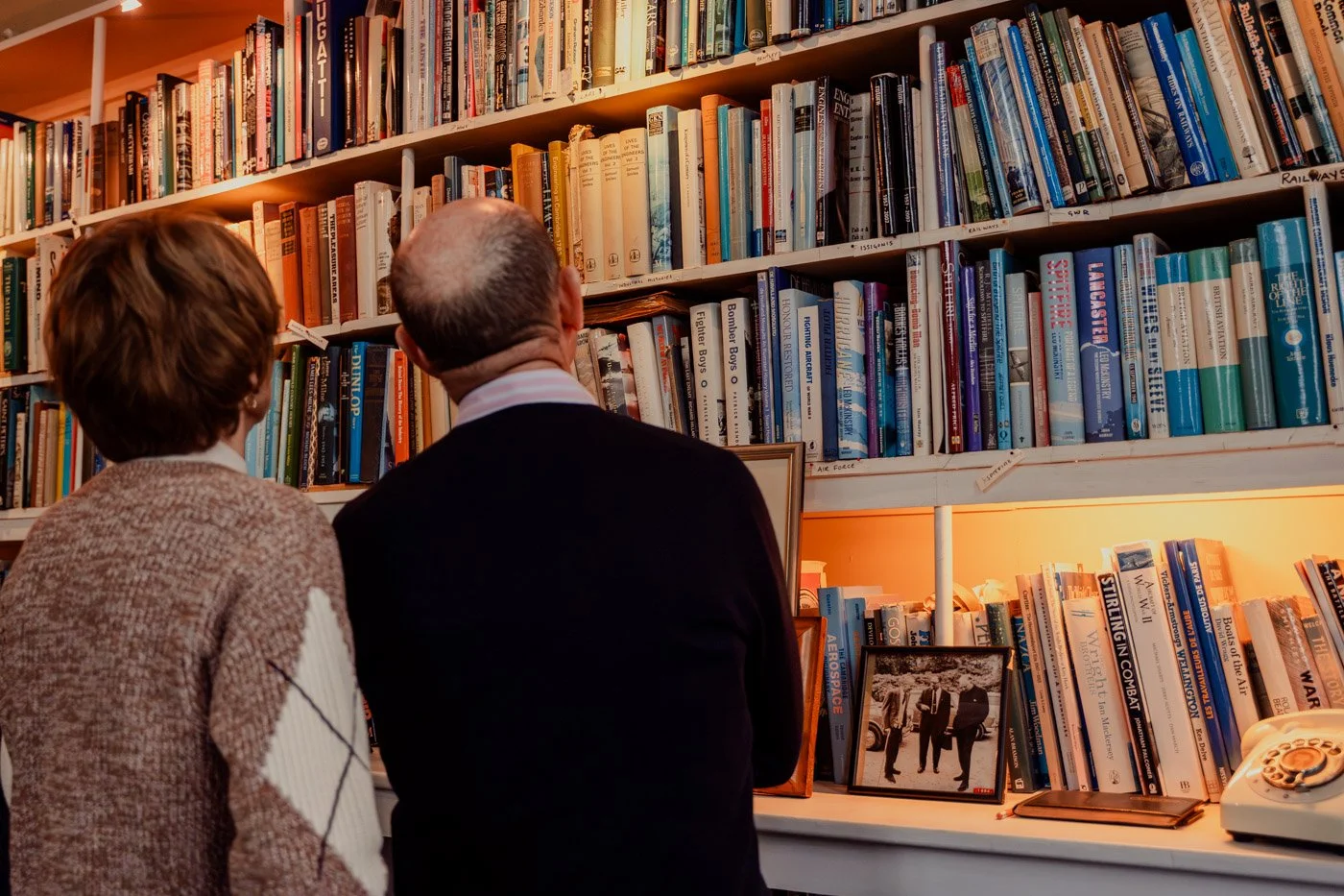 Comfortable seating area with two black leather lounge chairs with matching ottomans, gold cushions, a small wooden table, and stained glass windows with geometric patterns allowing sunlight to fill the room.