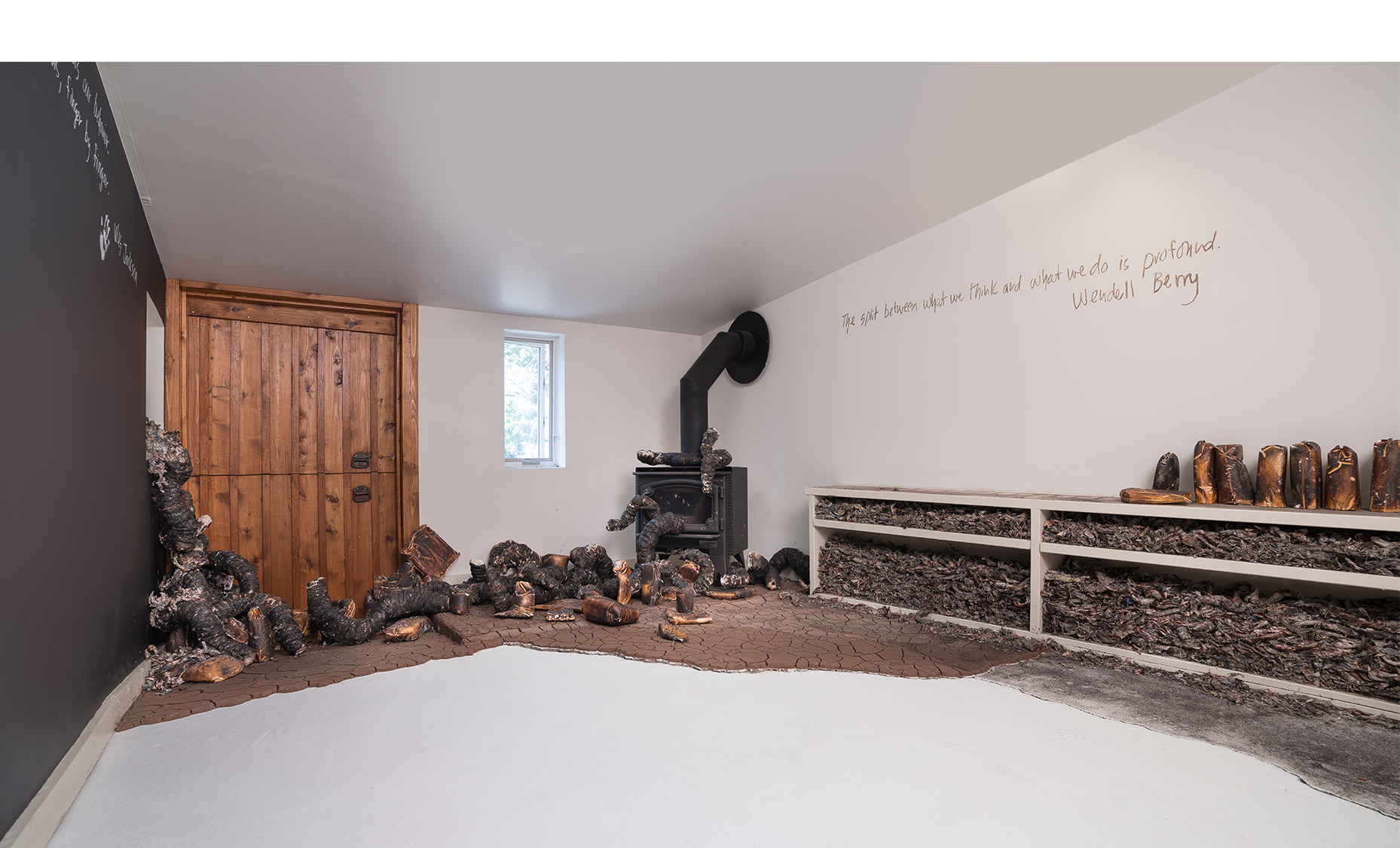 Seemingly Unconnected Events: The Writing is on the Wall/Heat, Drought & Fire Gallery , 2017, The Land Institute, Salina, Kansas. Charred newspaper and cast plaster organic forms with charred consumer goods casts, cracked earth, ash, charred newspaper fragments rammed into bookshelf. Wall texts with Kansas mud: writings of Wendell Berry, Wes Jackson and poet/sculptor Arna Radovich, collaborative blackboard for viewer/participants, gallery 15 x 11’.