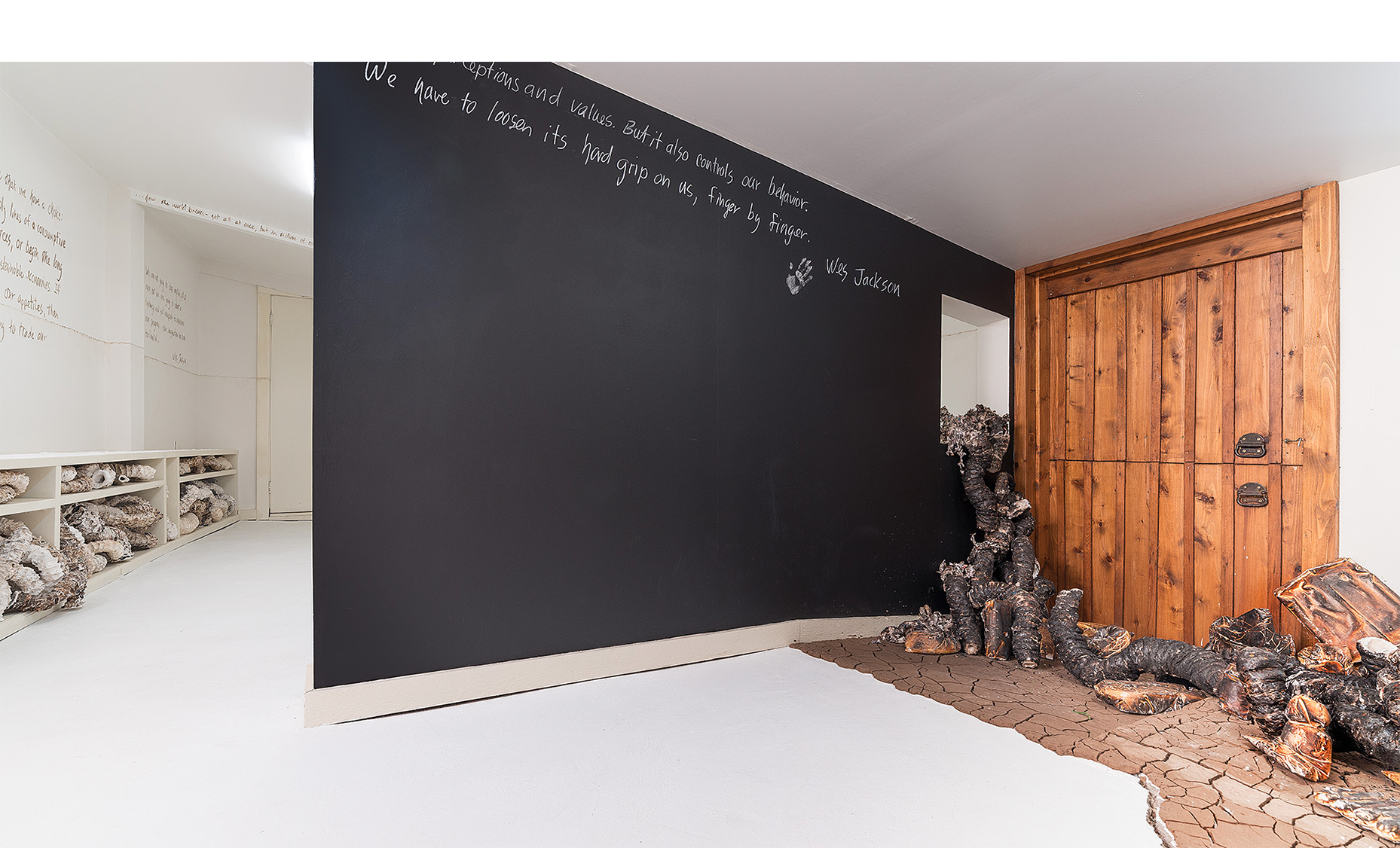  Installation detail of charred organic forms “climbing” through window, cracked earth and participatory blackboard wall with text by Wes Jackson. 