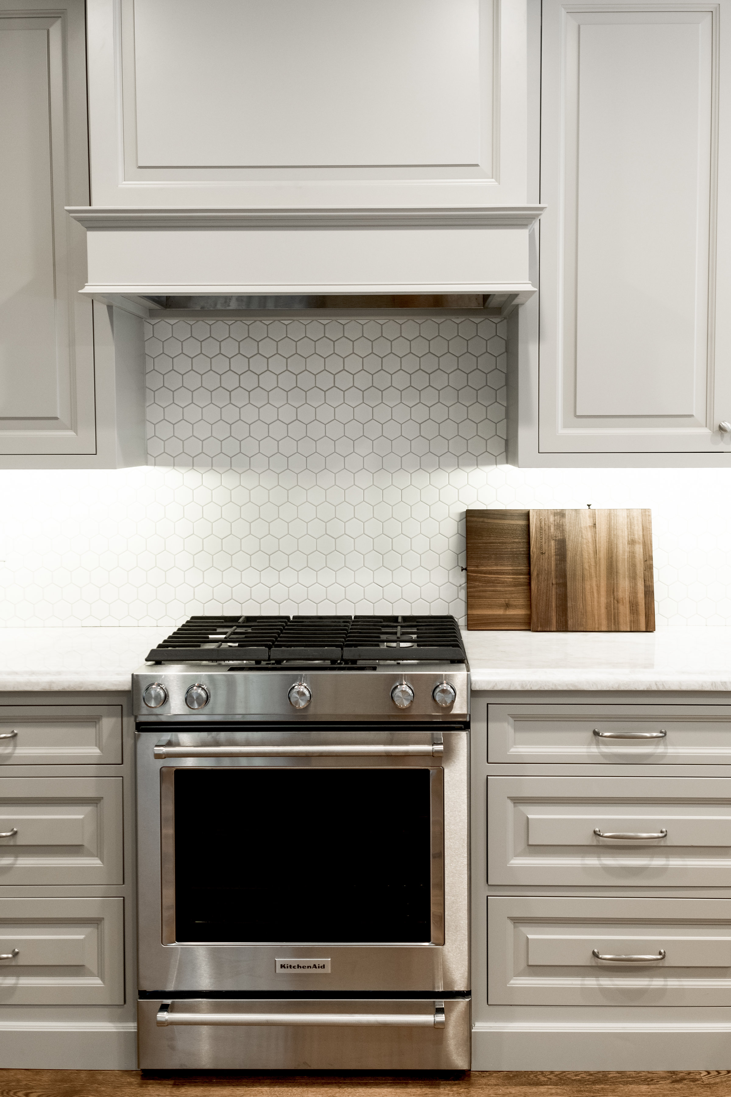 Taupe custom cabinets with chrome hardware and white hexagon tile