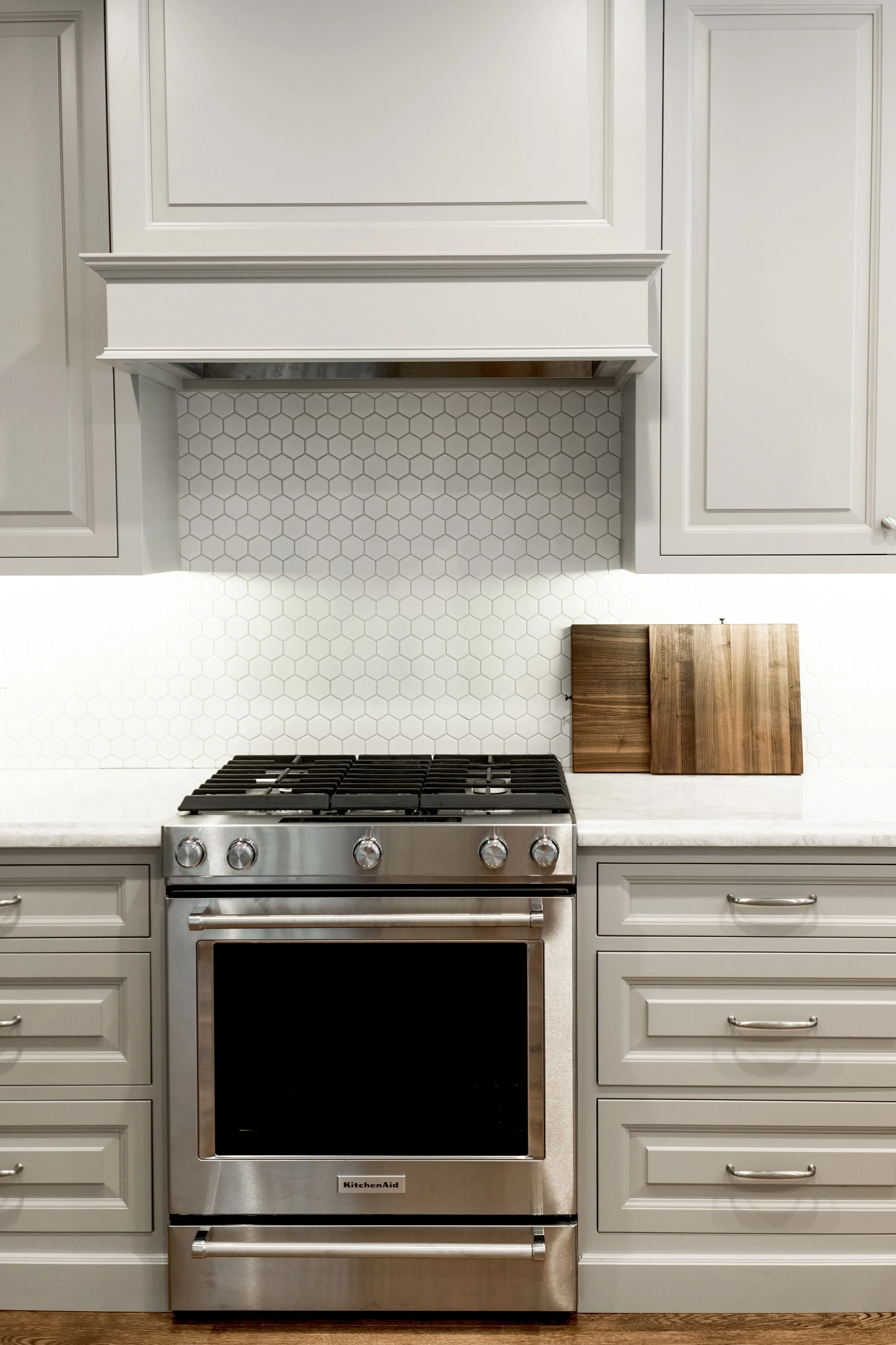 Taupe custom cabinets with chrome hardware and white hexagon tile