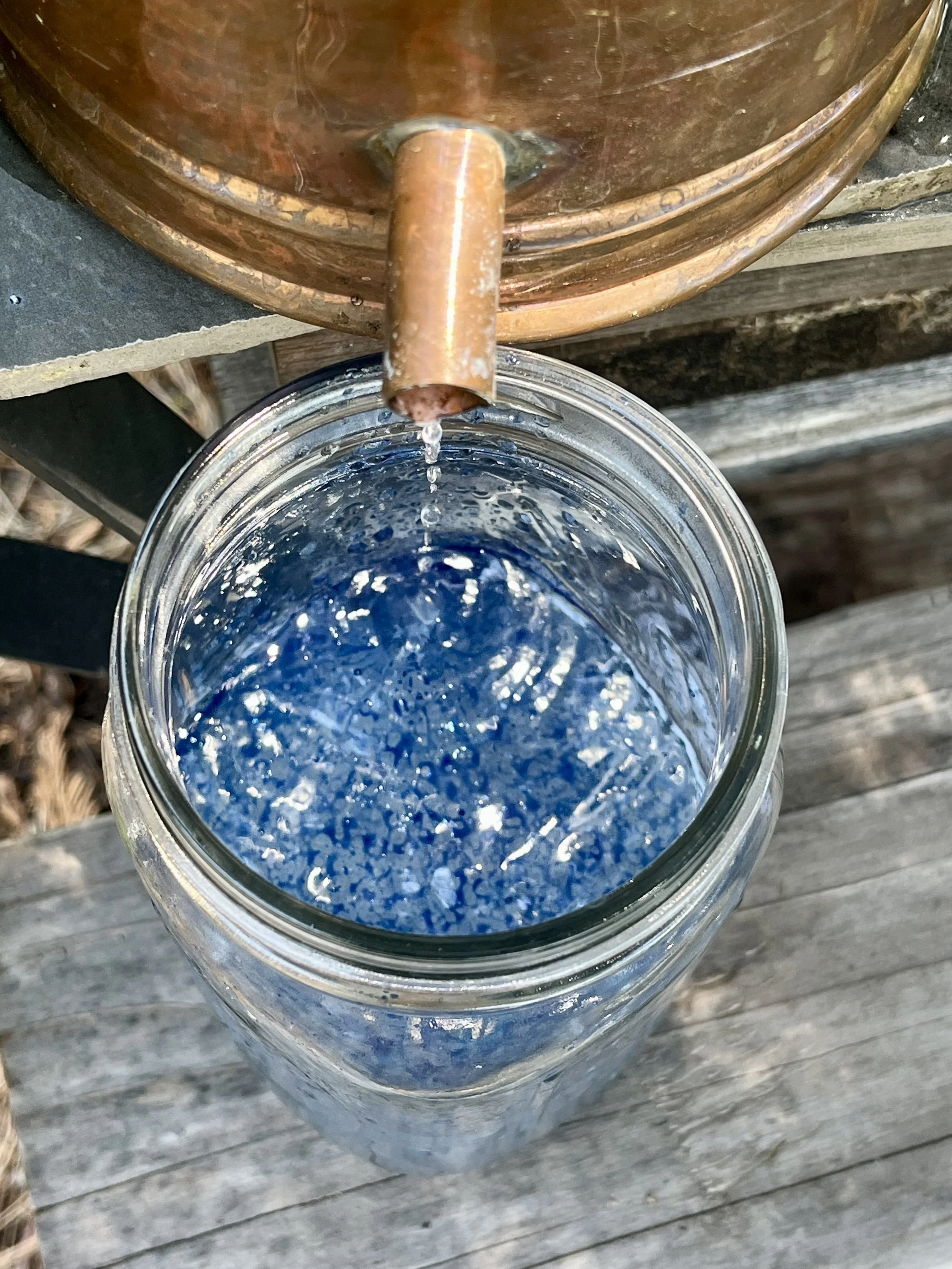 Water is being poured from a copper spigot into a glass jar filled with blue and purple decorative stones.