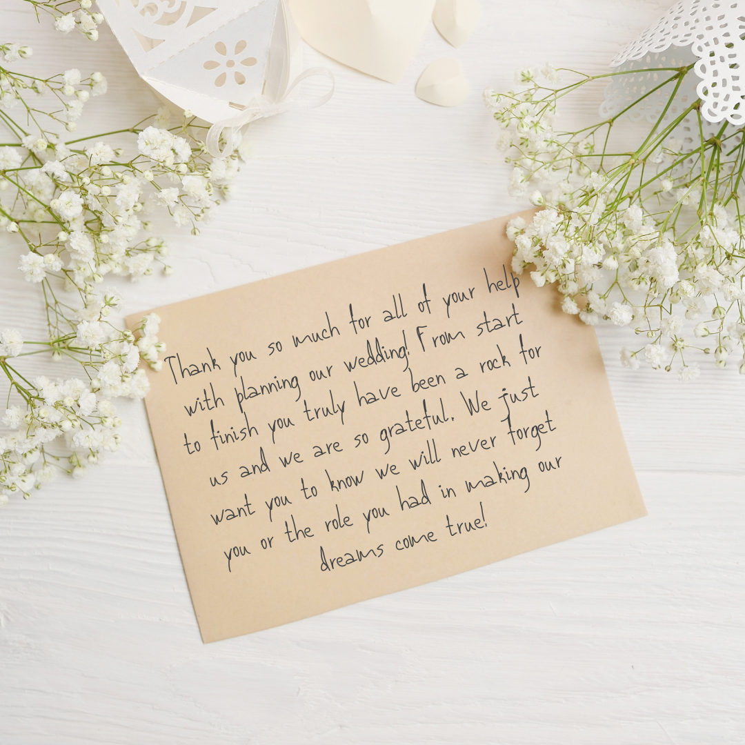 A handwritten thank you note on a beige card, surrounded by white flowers, with white decorative paper lanterns and flower arrangements in the background.