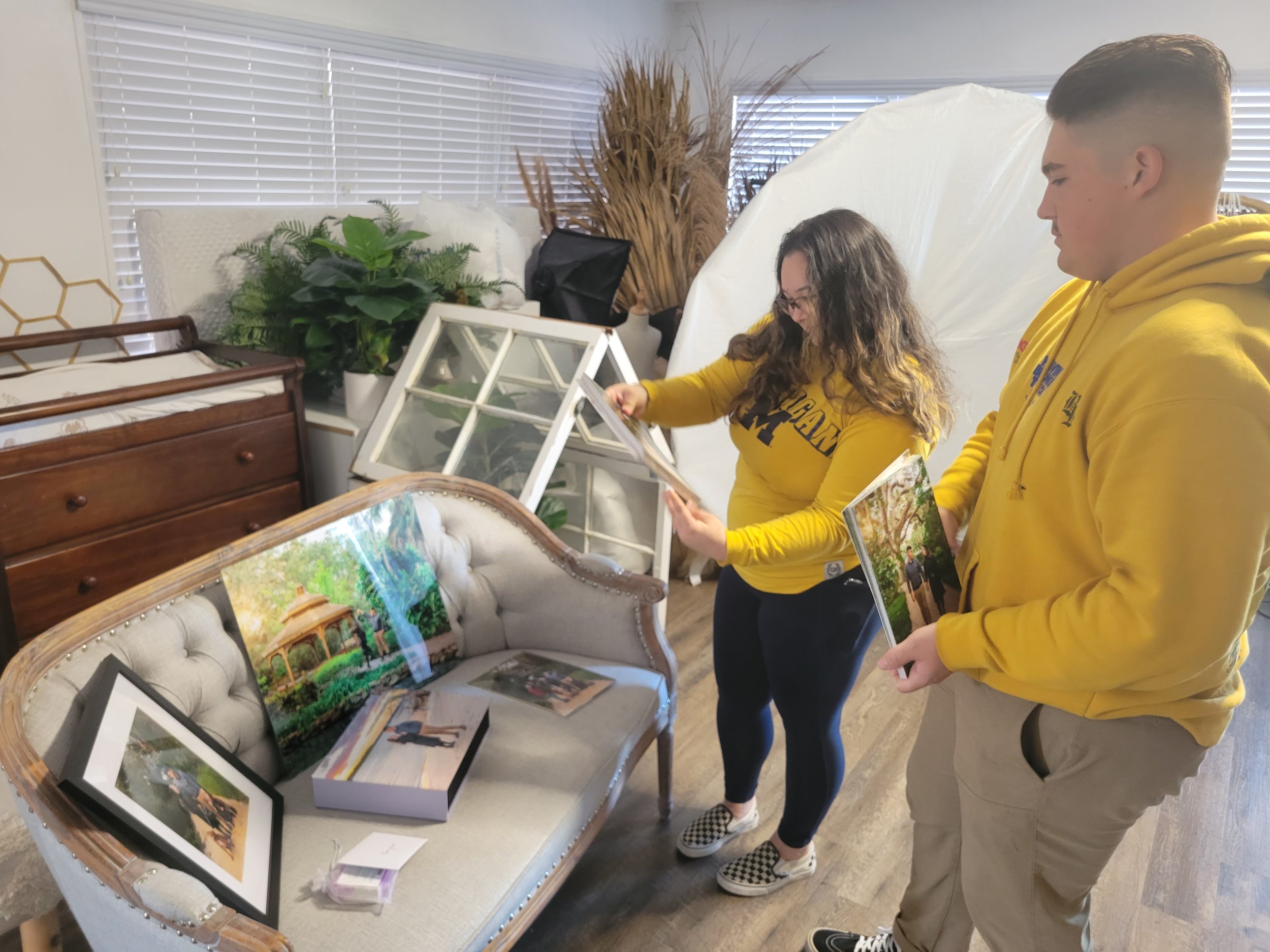 Young couple looking at wall art and photo albums after outdoor photo shoot in Palm Coast, FL at the park with natural light and their two dogs.