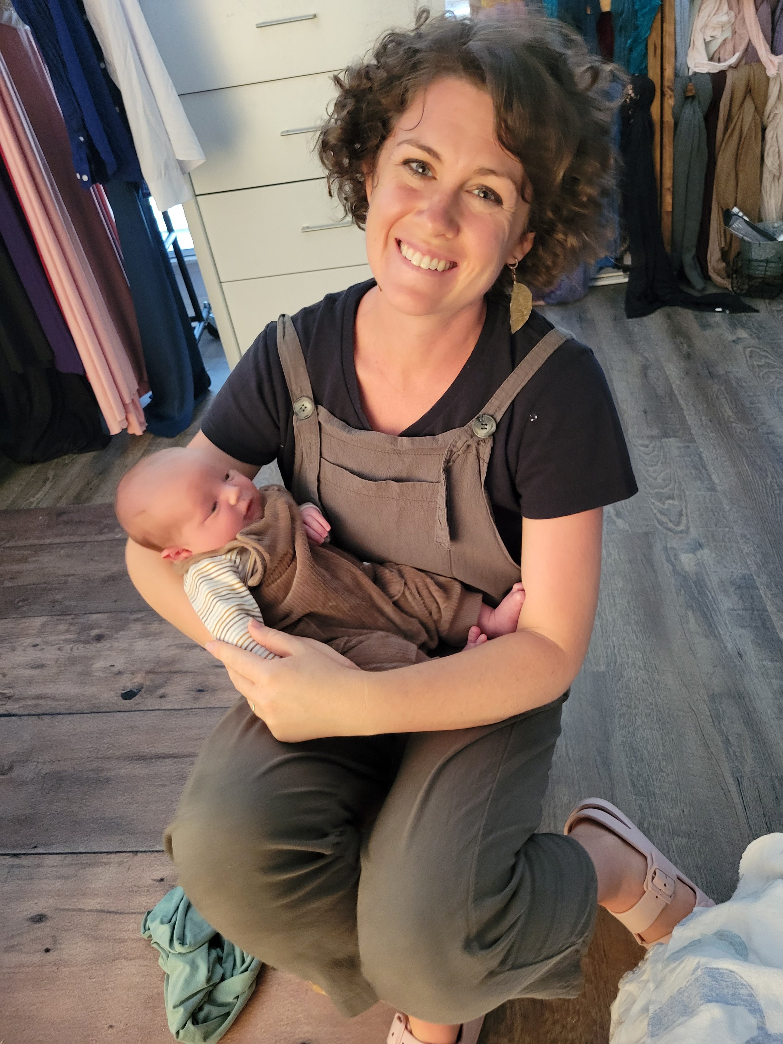 Jacksonville's best newborn photographer holding a newborn baby wrapped in a brown outfit with earth tones. The background features luxury clothes and boutique wooden furniture.