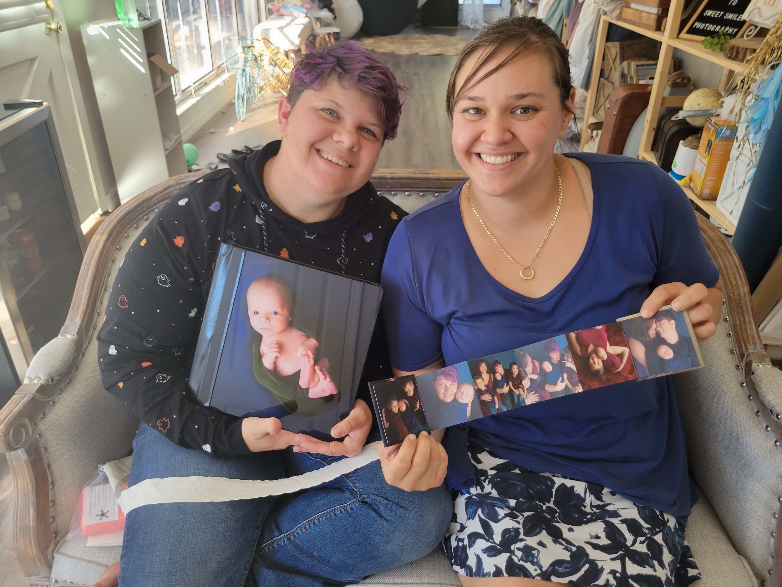 Same sex couple sitting in high end photo studio located in St. Augustine, FL looking at IVF newborn photo shoot pictures of baby boy and siblings.